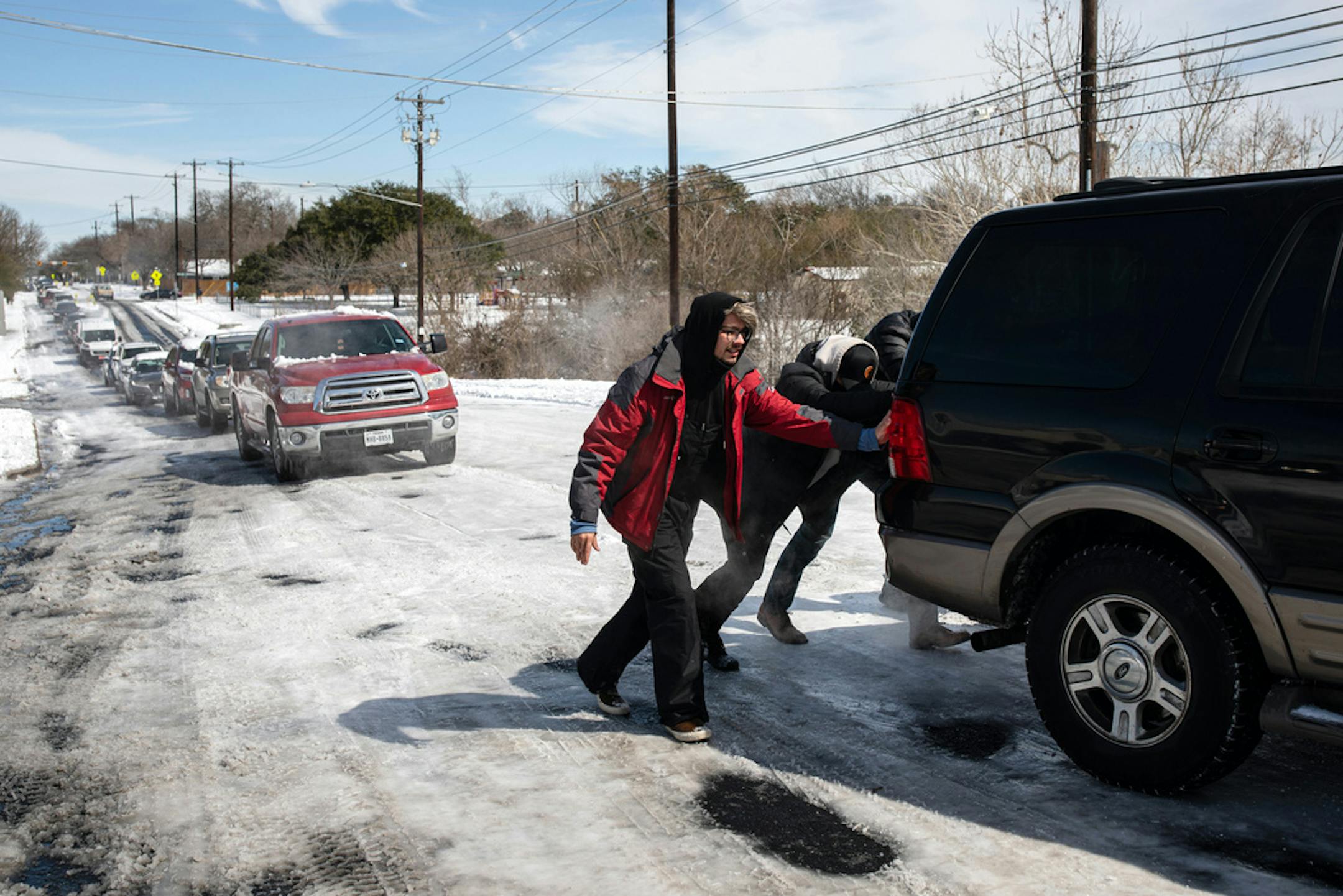 People help a motorist up a snow and ice-covered road on Tuesday, Feb. 16, 2021, in Austin, Texas. As a winter storm forced the Texas' power grid to the brink of collapse, millions of residents were plunged this week into darkness, bitter cold and indignation over being stuck in uncomfortable and even dangerous conditions. (Tamir Kalifa/The New York Times)