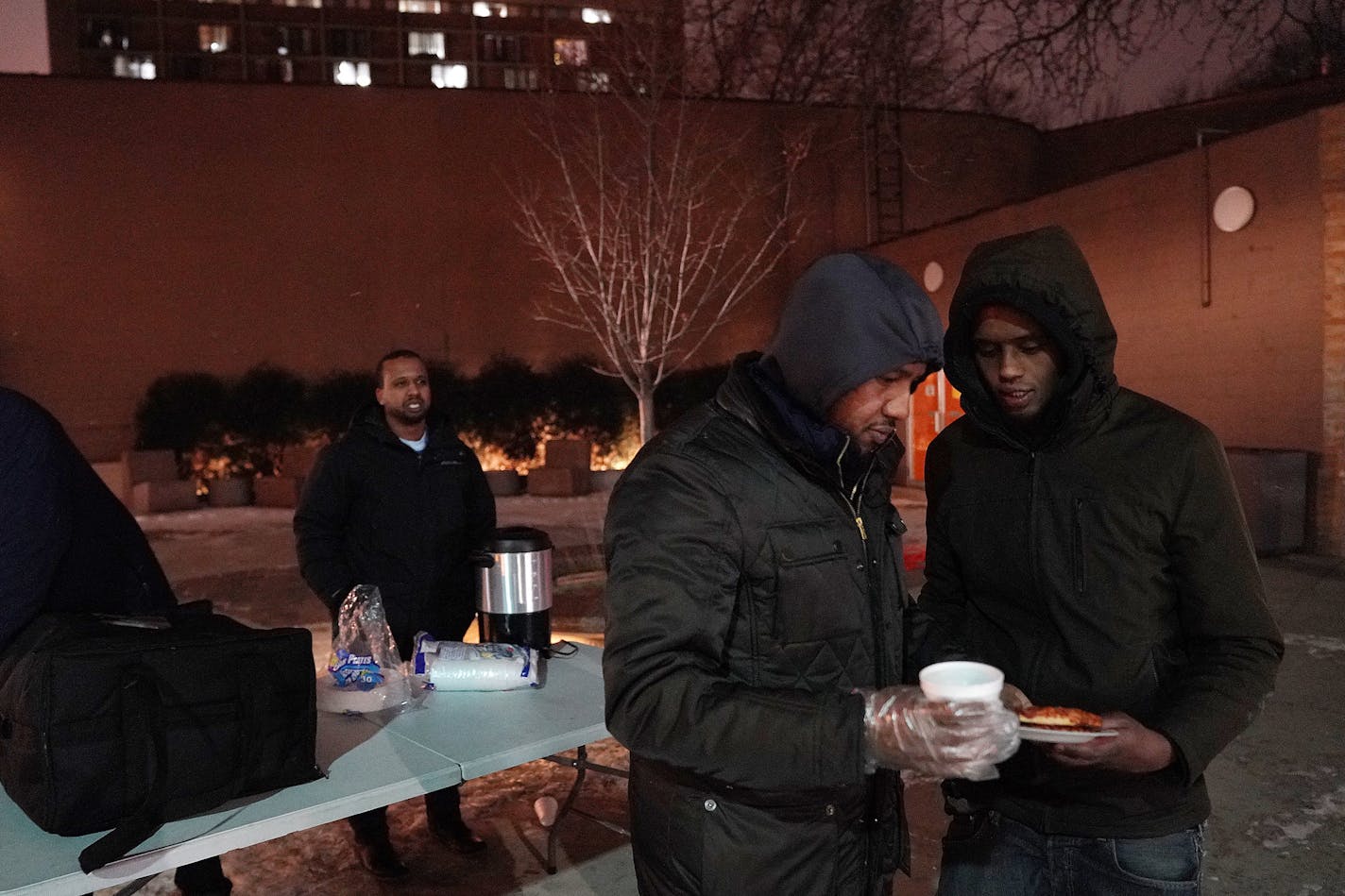 Abdirahman Mukhtar spoke with a man as he and Abdullahi Farah, left, gave out pizza and tea to young people from a stand Friday in the Cedar-Riverside neighborhood. ] ANTHONY SOUFFLE &#x2022; anthony.souffle@startribune.com A group of Somali volunteers including Abdirahman Mukhtar, Abdullahi Farah, and Mahdi Abdi gave out pizza and tea to young people from a stand Friday, Dec. 28, 2018 in the Cedar-Riverside neighborhood of Minneapolis. The men hope by connecting with youth and engaging them in