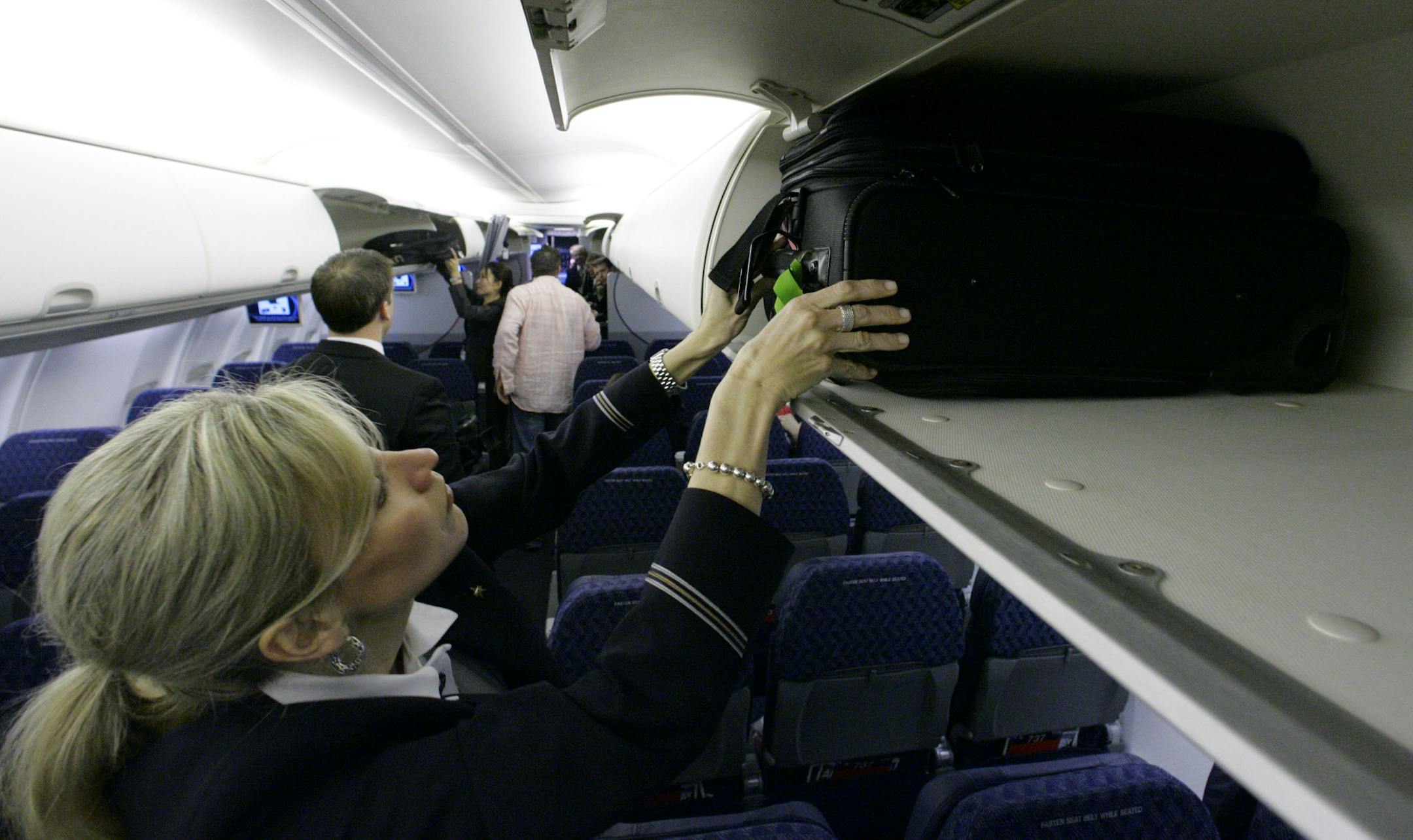 FILE - In this April 13, 2009 file photo, American Airlines flight attendant Renee Schexnaildre demonstrates the overhead baggage area during a media preview of the airline's new Boeing 737-800 jets, at Dallas Fort Worth International Airport in Grapevine, Texas.