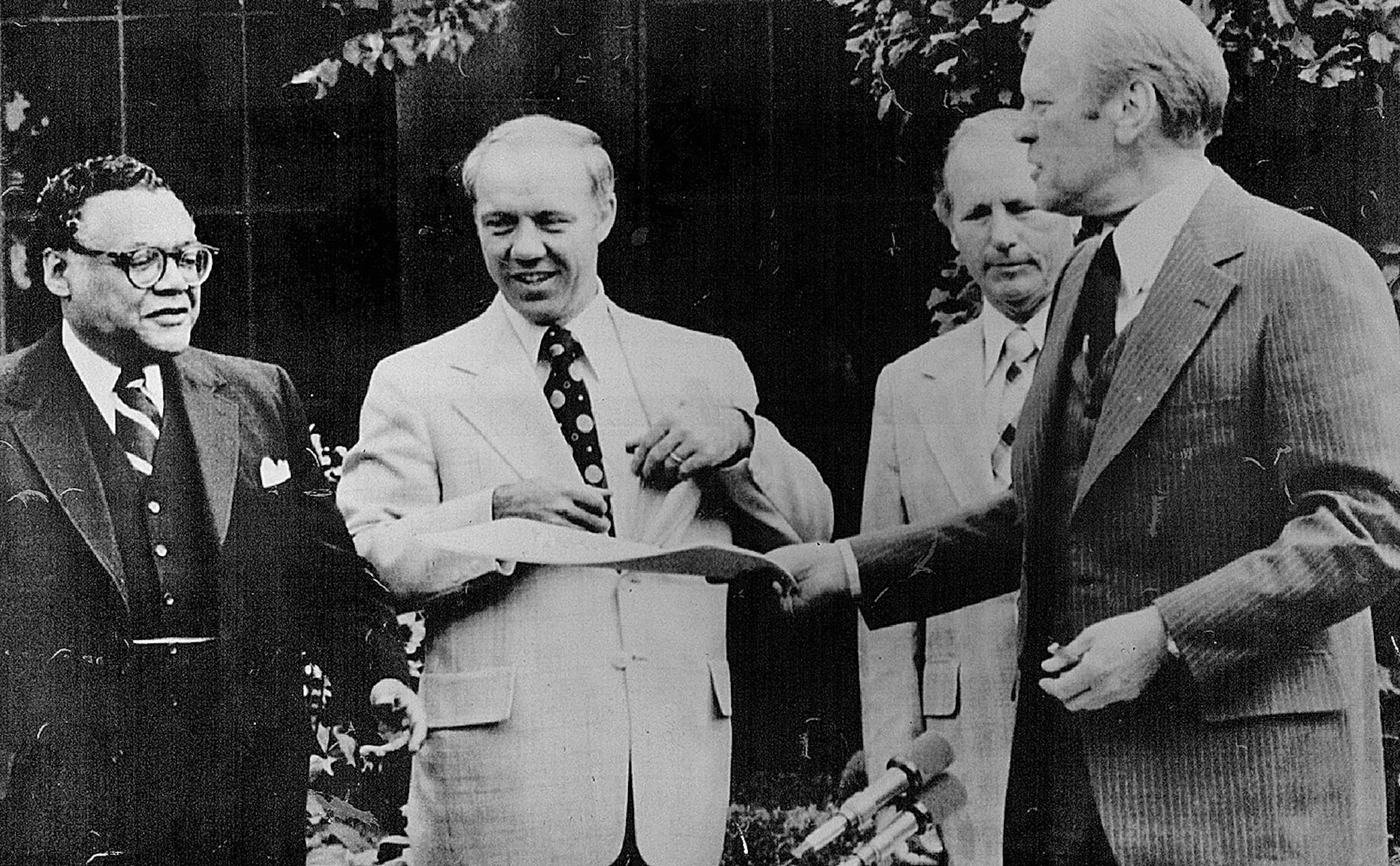 July 12, 1976 After The Singing -- President ford hands a copy of a bill he just signed to transportation secretary William coleman in the white House Rose garden Monday. The presudent signed a four -year commercial aviation development. Bill that he say will make possible thousands of jobs." Next to coleman is Rep. James Oberstar, D-Minn behind ford is rep. William Hersen R-Ohio. AP Wirephoto