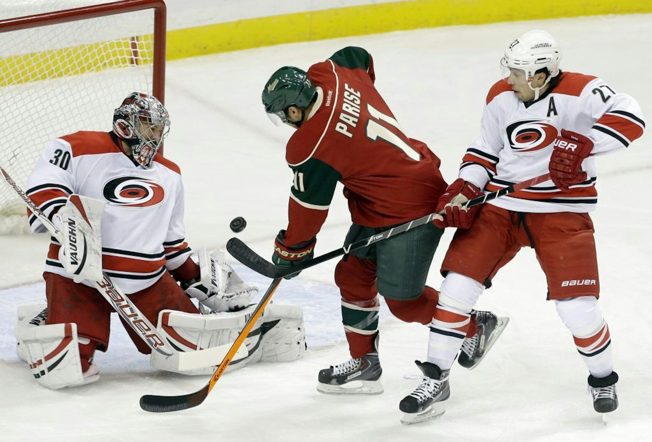 Carolina Hurricanes goalie Cam Ward, left, blocks a shot off the stick of Minnesota Wild's Zach Parise, center, as Hurricanes' Justin Faulk defends in the first period of an NHL hockey game Thursday, Oct. 24, 2013, in St. Paul, Minn.