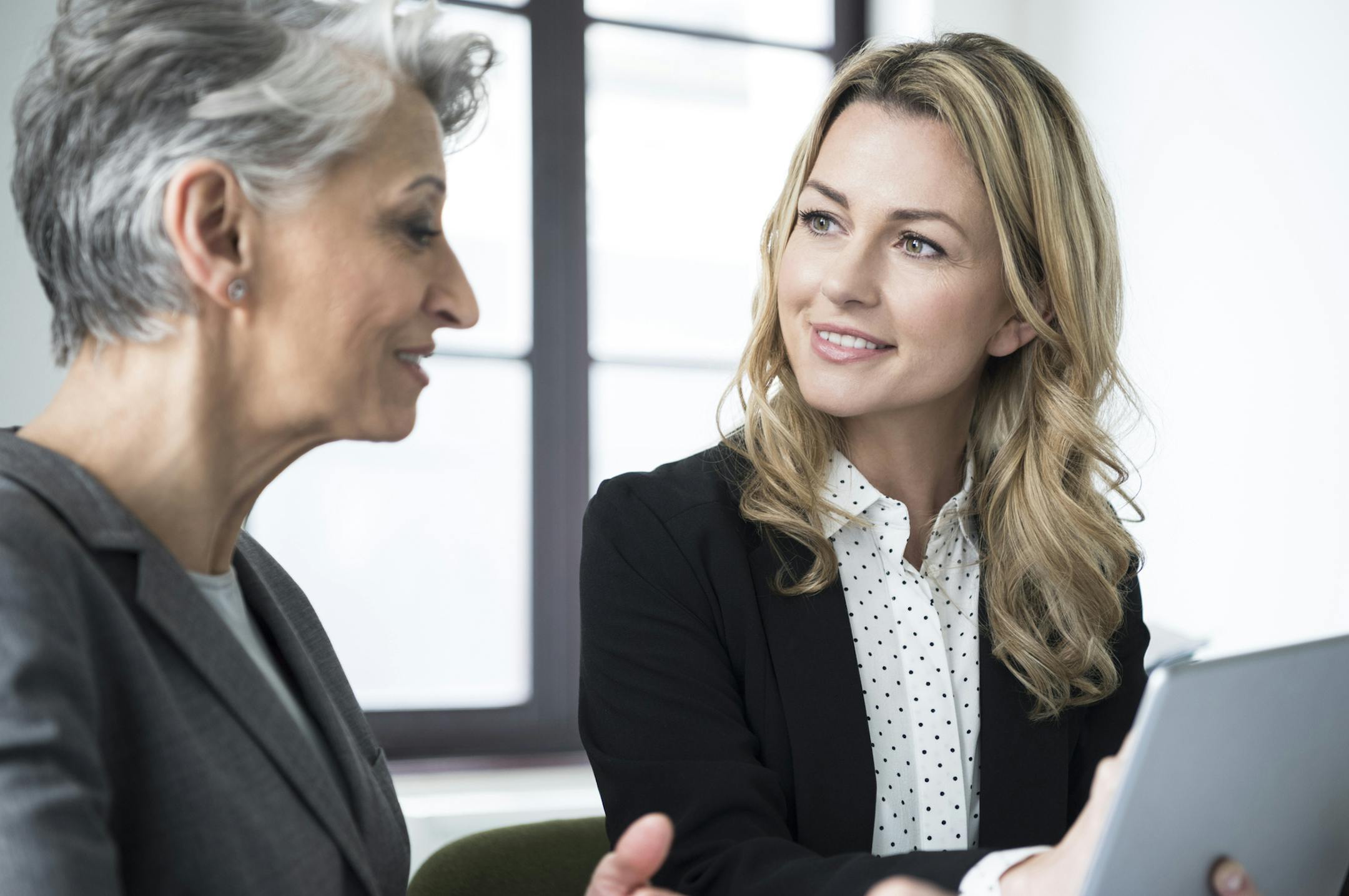 Attractive mid adult businesswoman with long blonde hair talking to mature colleague with short grey hair in office. istock photo