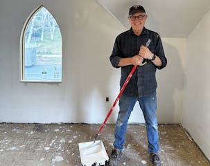 The man who led the effort to renovate a vacant house stands next to a pail of paint he was using on the walls.