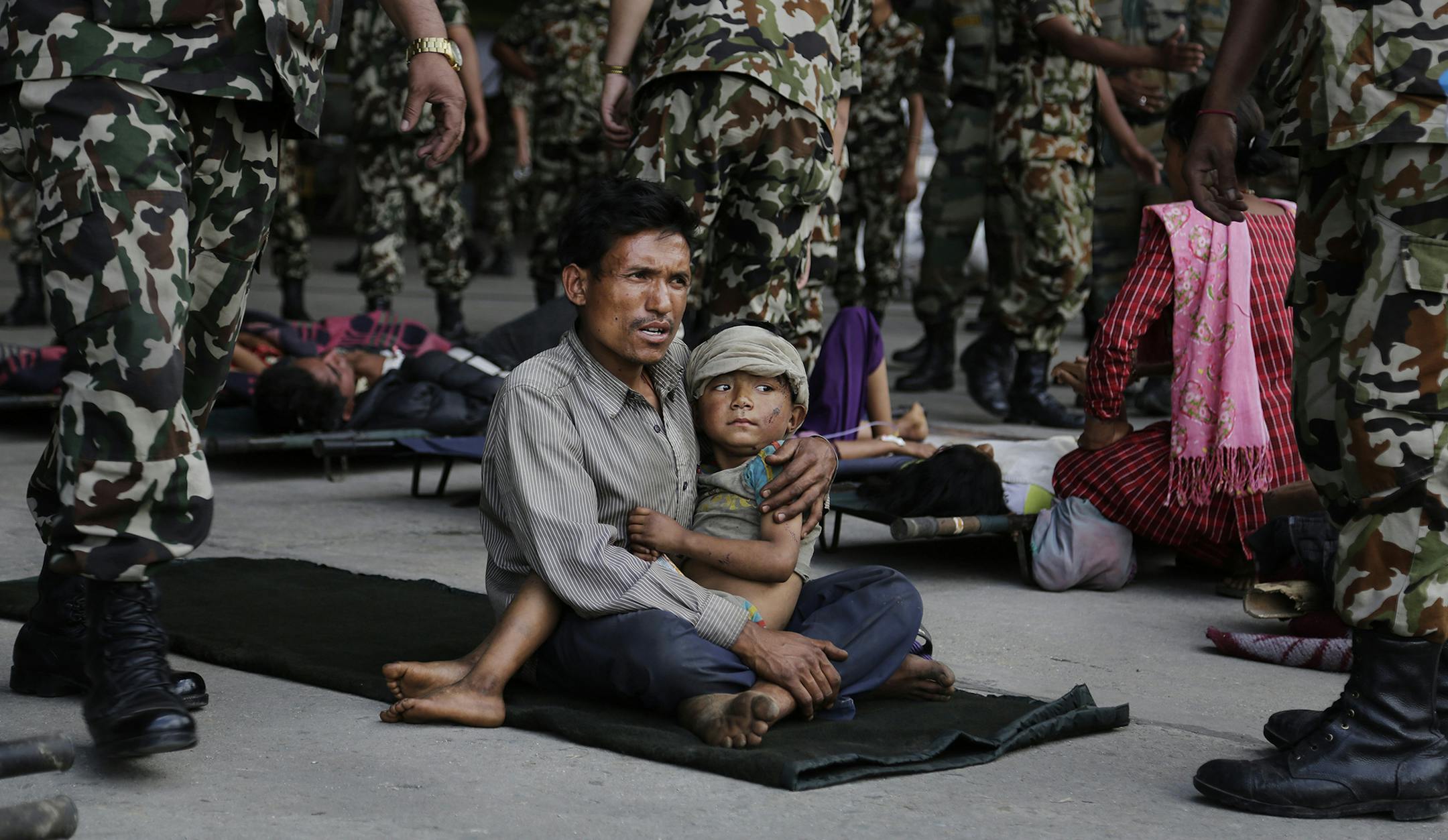 A man sits with a child on his lap as victims of Saturdayís earthquake, wait for ambulances after being evacuated at the airport in Kathmandu, Nepal, Monday, April 27, 2015. The death toll from Nepal's earthquake is expected to rise depended largely on the condition of vulnerable mountain villages that rescue workers were still struggling to reach two days after the disaster. (AP Photo/Altaf Qadri) ORG XMIT: MIN2015042716131473