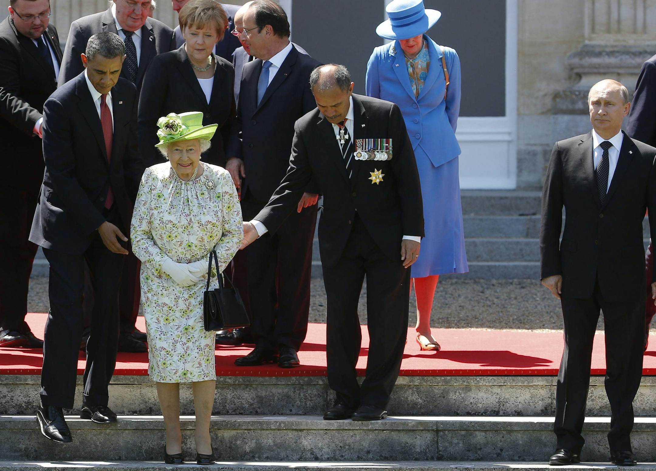Russian President Vladimir Putin stands at right as U.S. President Barack Obama and New Zealand's Governor-General Jerry Mateparae guide Queen Elizabeth II to her position for a group photo as French President Francois Hollande, center, and German Chancellor Angela Merkel, talk, center, as they take part in the 70th anniversary of D-Day in Benouville in Normandy, France, Friday, June 6, 2014. (AP Photo/Charles Dharapak)