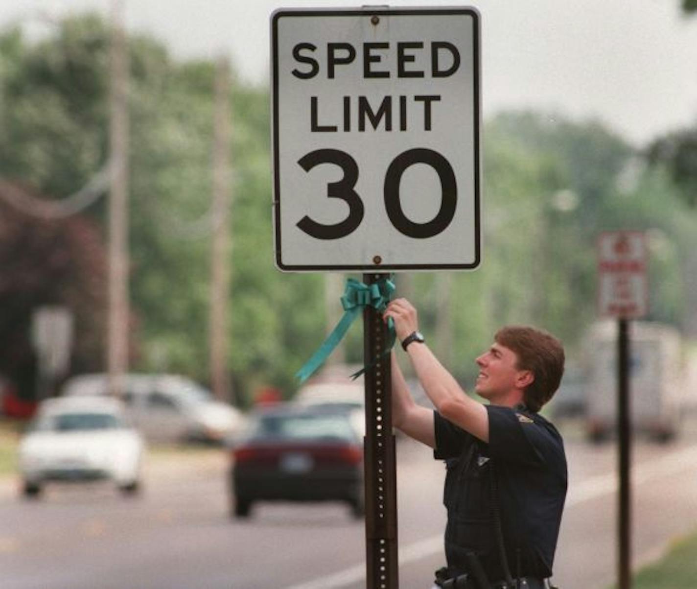 Brooklyn Park police officer Todd Kanieski attataches a ribbon to a speed limit sign to remind drivers to drive safely this 4th of July weekend. -- Brooklyn Park police officer Todd Kanieski attataches a ribbon to a speed limit sign to remind drivers to drive safely this 4th of July weekend.