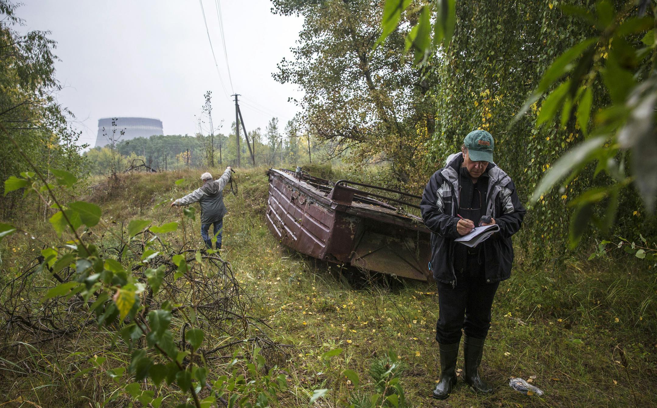 A cooling tower of the Chernobyl Nuclear Power Plant emerges from the forest in the distance as Timothy Mousseau, a biologist, right, measures bat sounds with his assistant in the exclusion zone around the plant in Ukraine, Sept. 19, 2013. A long-term study by Mousseau of birds in the area has found that some species have adapted to the radioactive environment by producing more protective antioxidants, with correspondingly less genetic damage. (William Daniels/The New York Times) ORG XMIT: XNYT5