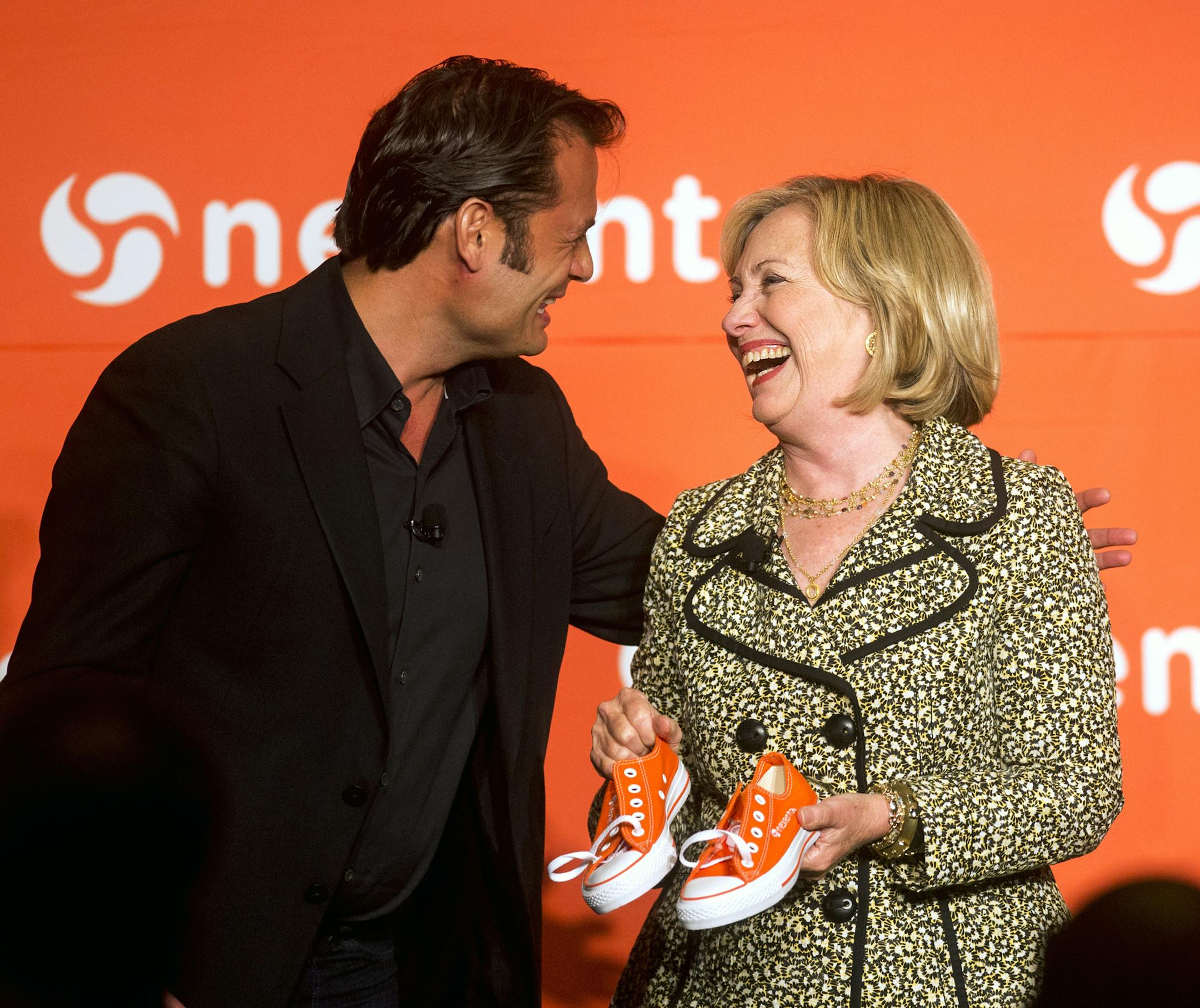 Nexenta CEO Tarkan Maner, left, presents former Secretary of State Hillary Rodham Clinton with a pair of his company's trademark orange sneakers during the Nexenta OpenSDx Summit Thursday, Aug. 28, 2014, in San Francisco. (AP Photo/Noah Berger)