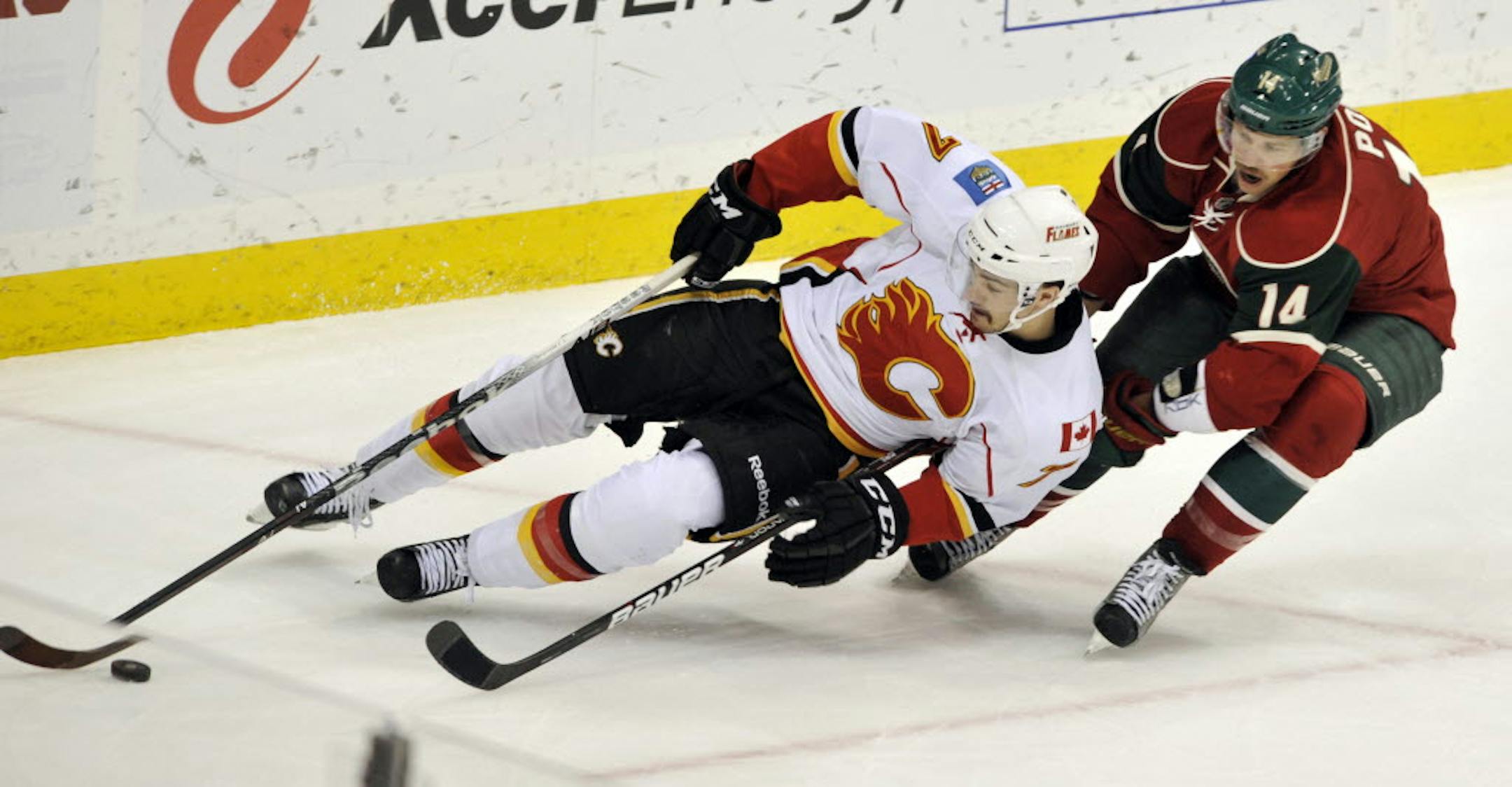 Calgary's J.T. Brodie, left, goes to the ice while chasing the puck with Minnesota's Darroll Powe.