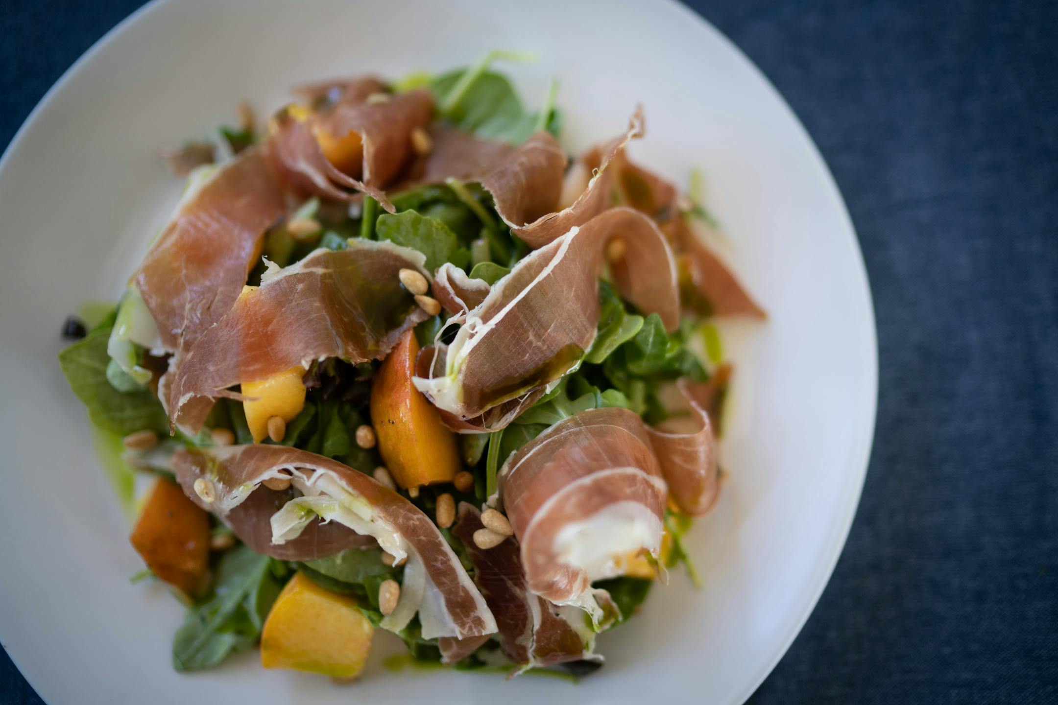 The antipasti peaches and prosciutto; fresh peaches tossed with prosciutto, arugula, pine nuts, and basil oil at Gia at the Lake.