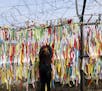 A woman hangs a ribbon wishing for the reunification of the two Koreas on a fence at the Imjingak Pavilion in Paju, South Korea, near the border with 