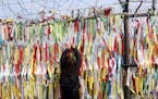 A woman hangs a ribbon wishing for the reunification of the two Koreas on a fence at the Imjingak Pavilion in Paju, South Korea, near the border with 