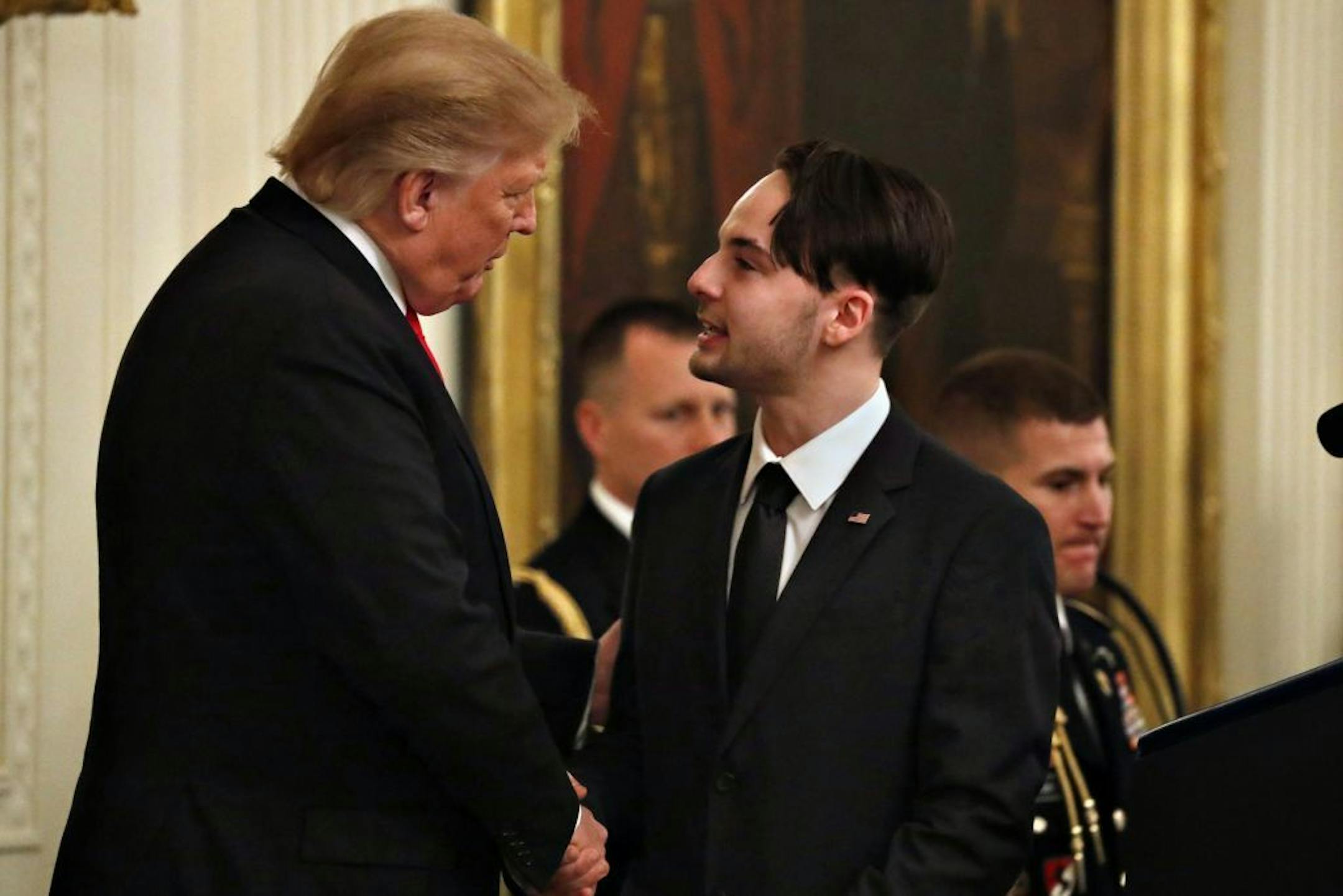 President Donald Trump shakes hands with Trevor Oliver, 22, before awarding the Medal of Honor to Oliver's father, Army Staff Sgt. Travis Atkins, with Oliver accepting the posthumous recognition for conspicuous gallantry in Iraq in June 2007, in the East Room of the White House, Wednesday March 27, 2019, in Washington. Atkins died while engaged in hand-to hand combat with a suspected insurgent before noticing that his opponent was about to trigger a suicide vest strapped to his body, subsequentl