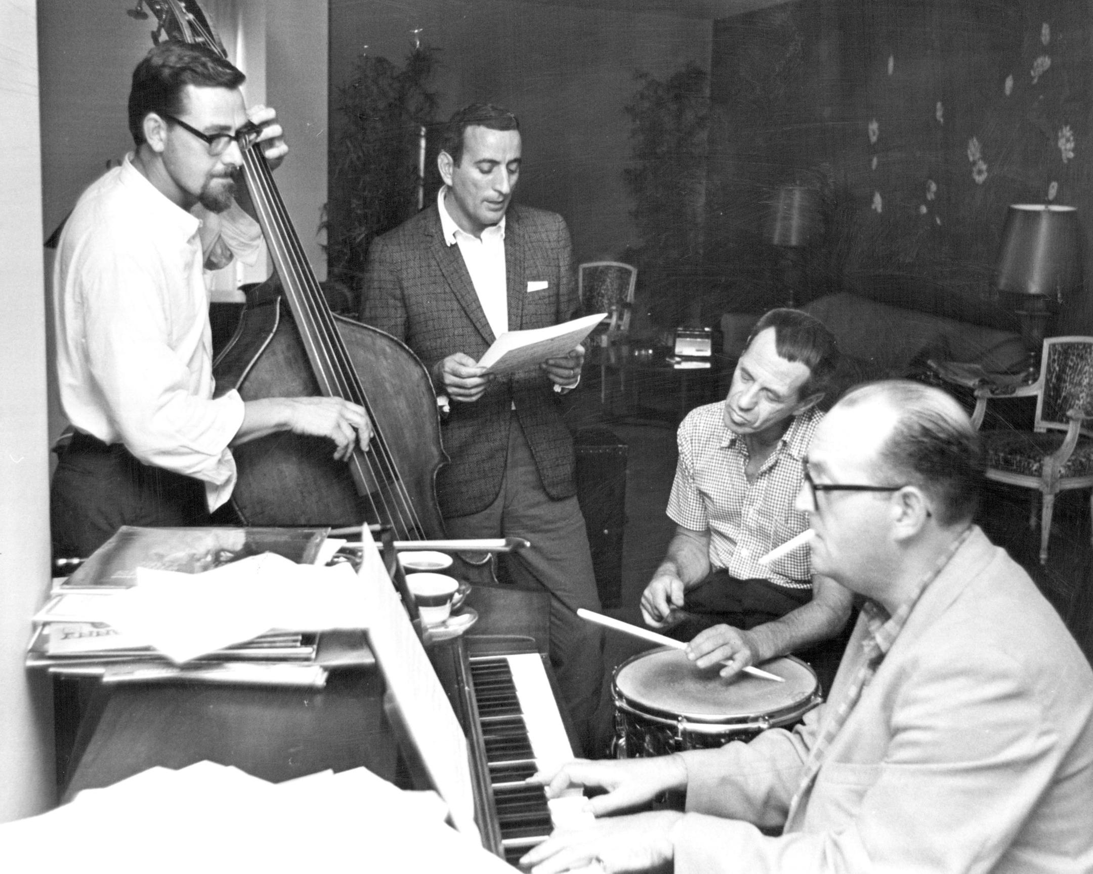 Tony Bennett rehearses 'How Insensitive' on Aug. 21, 1964. Ralph Sharon was at the piano, Billy Eximer at drums, singer Tony Bennett leaned against a wall and stared through the smoke of his cigarette at a small tape recorder on the table. Around the table sat the Ralph Sharon Trio - pianist Ralph Sharon, bass player Hal Gaylor and drummer Billy Eximer. He and the trio will appear with Duke Ellington and his orchestra at 8 p.m. on Aug. 22 at Metropolitan Stadium. Bennett arrived in Minneapolis a few days early to check the stage, lighting, microphones, and acoustics.