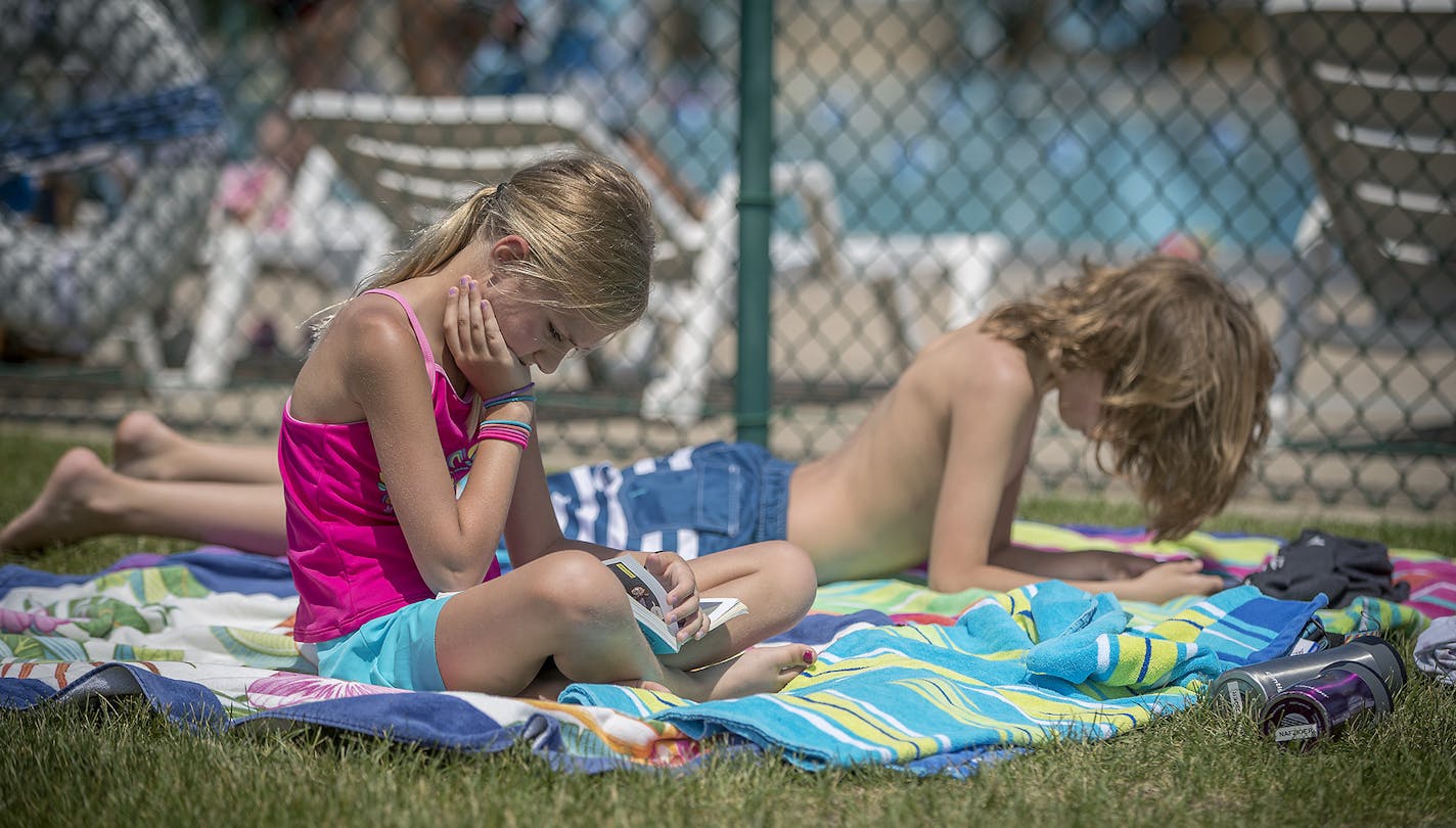 Adam Nafziger's children, Freya, 9, left, and Linus, 11, right, read their books as they waited for the pool to open from a break at the Richfield pool, Thursday, June 14, 2018 in Minneapolis, MN.