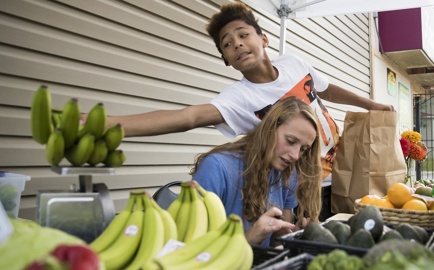 High school student Lunden Woodberry (CQ), 14, reached over Nicole Herrli (CQ), 22, a senior at St. Thomas University, as he weighed a bunch of bananas at a Brightside Produce stand outside Fremont Market as part of an unusual collaboration between the University of St. Thomas and corner stores in North Minneapolis on August 7, 2017 in Minneapolis, Minn. ] RENEE JONES SCHNEIDER &#xef; renee.jones@startribune.com ORG XMIT: MIN1708081317450841