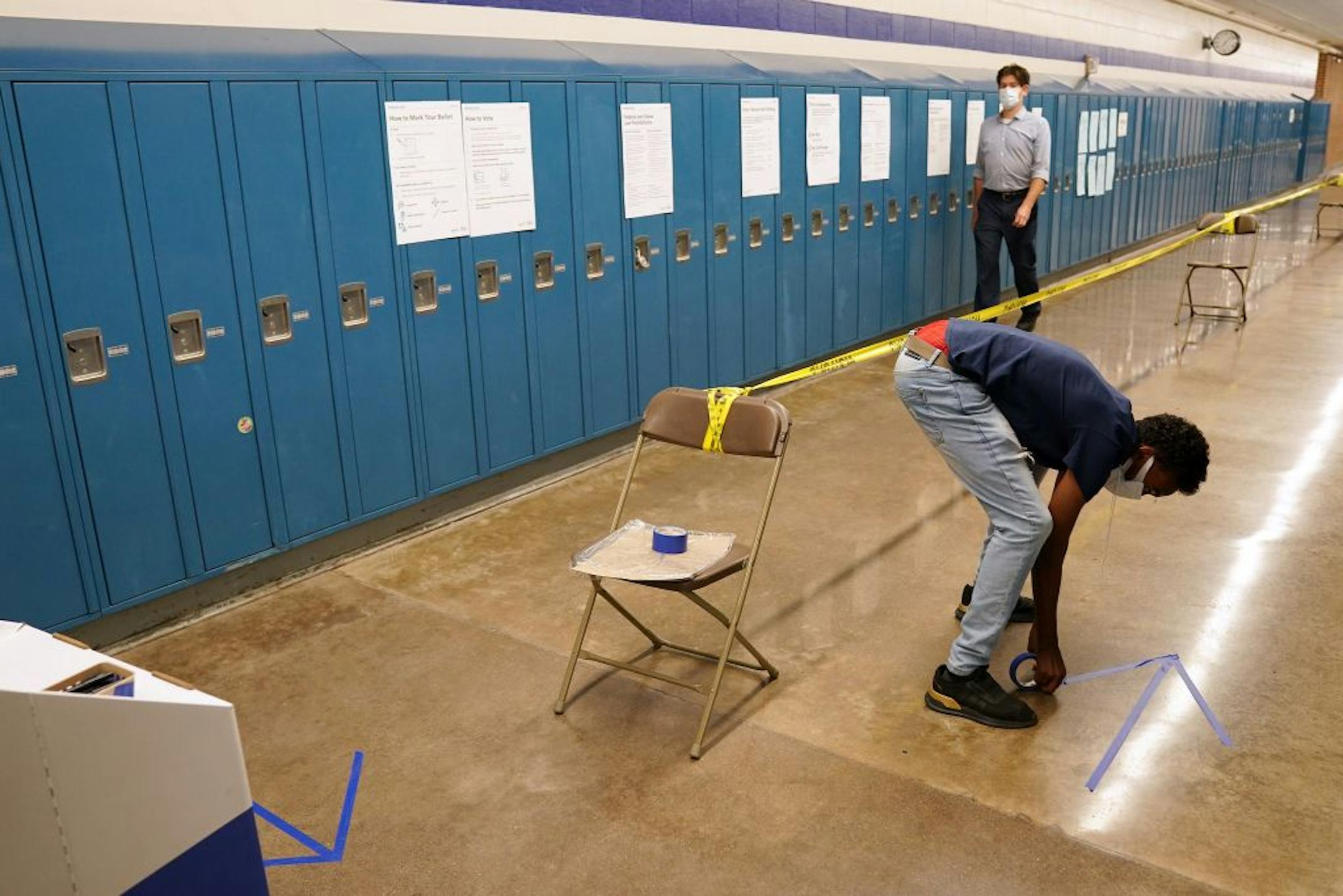 Abdilahi Abdi used to tape to mark off one way foot traffic for voters to encourage social distancing as they cast their ballots Tuesday morning at Northeast Middle School in Minneapolis.