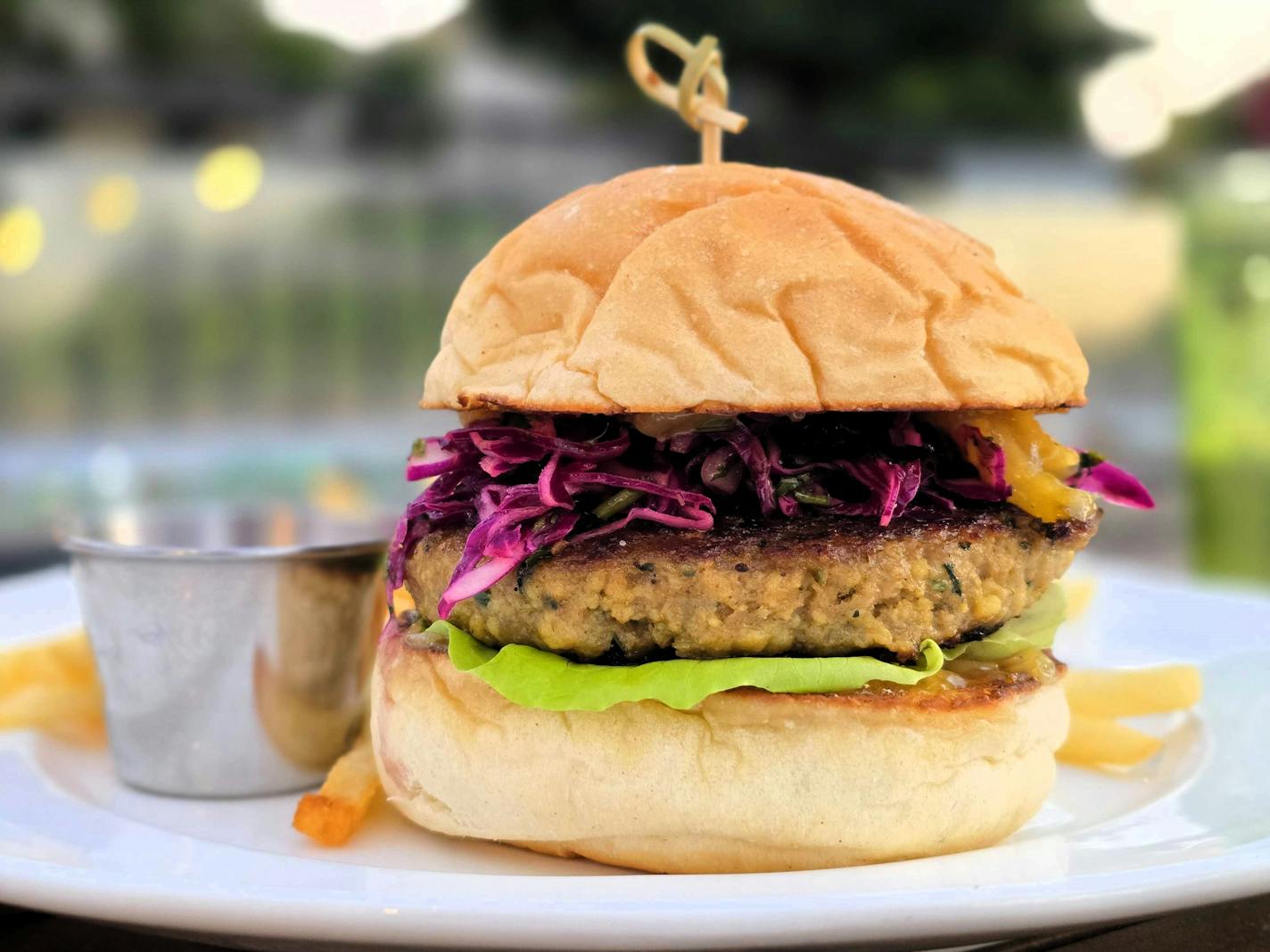 A side-view look at a burger with red slaw and a bright green leaf of lettuce, shot on a patio