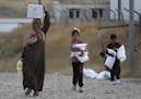 A Syrian woman and her children, who were displaced by the Turkish military operation in northeastern Syria, carry food supplies at the Bardarash refu