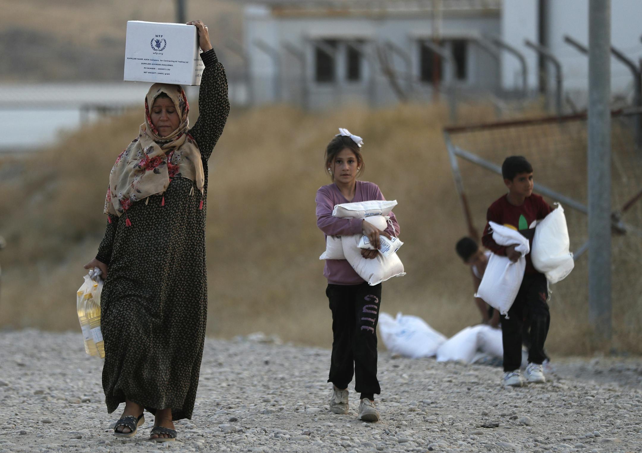 A Syrian woman and her children, who were displaced by the Turkish military operation in northeastern Syria, carry food supplies at the Bardarash refugee camp, north of Mosul, Iraq, Thursday, Oct. 17, 2019. Hundreds of refugees have crossed into Iraq in the past week, mostly through unofficial border points. On Wednesday, a first group of 890 people were bused to the Bardarash camp, in northern Iraq's semi-autonomous Kurdish region, which up until two years ago housed displaced people from the I