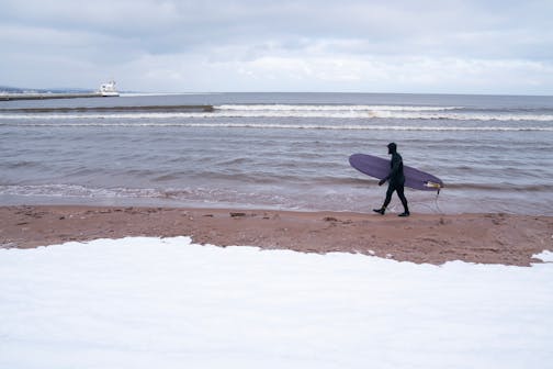 A surfer walked along the snow-covered shore of Lake Superior in Duluth on a January day.