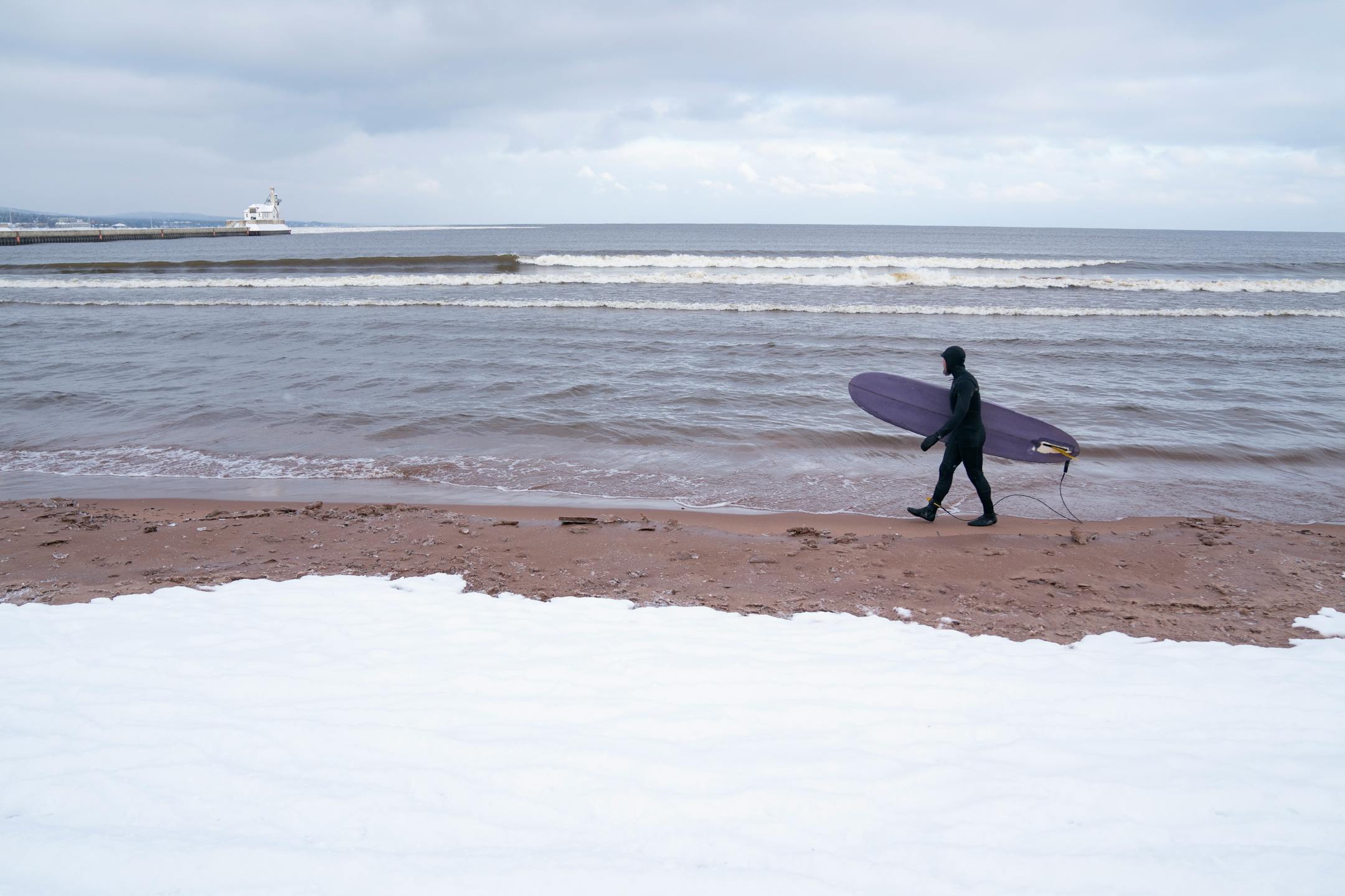 A surfer walked along the snow-covered shore of Lake Superior in Duluth on a January day.