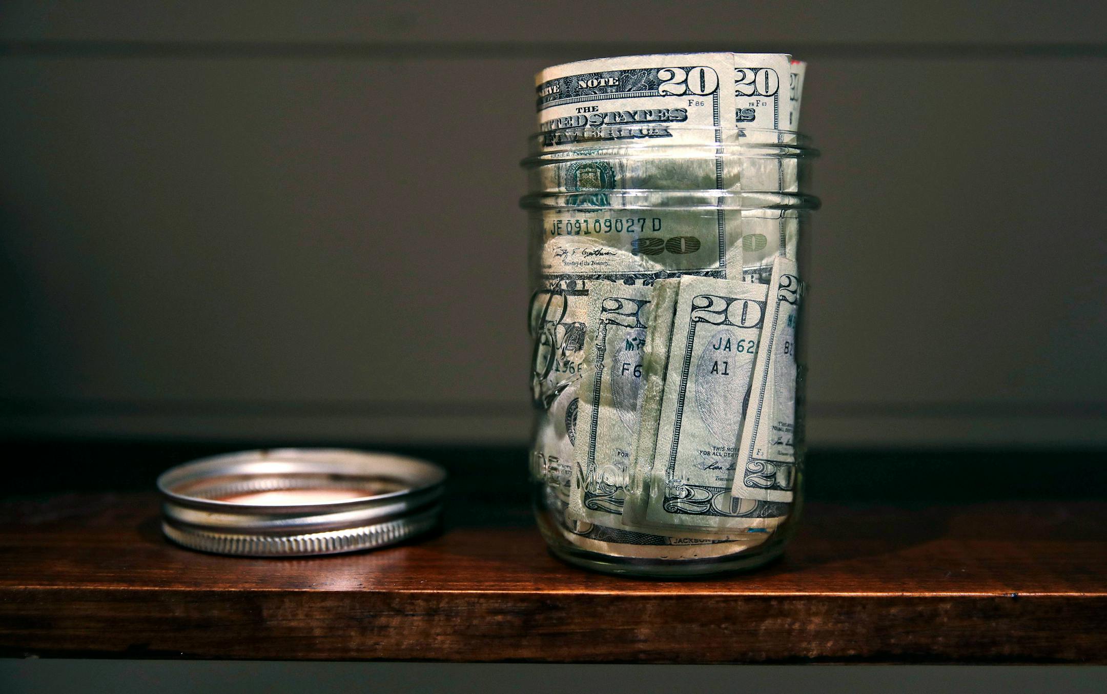 A canning jar filled with currency sits on a shelf