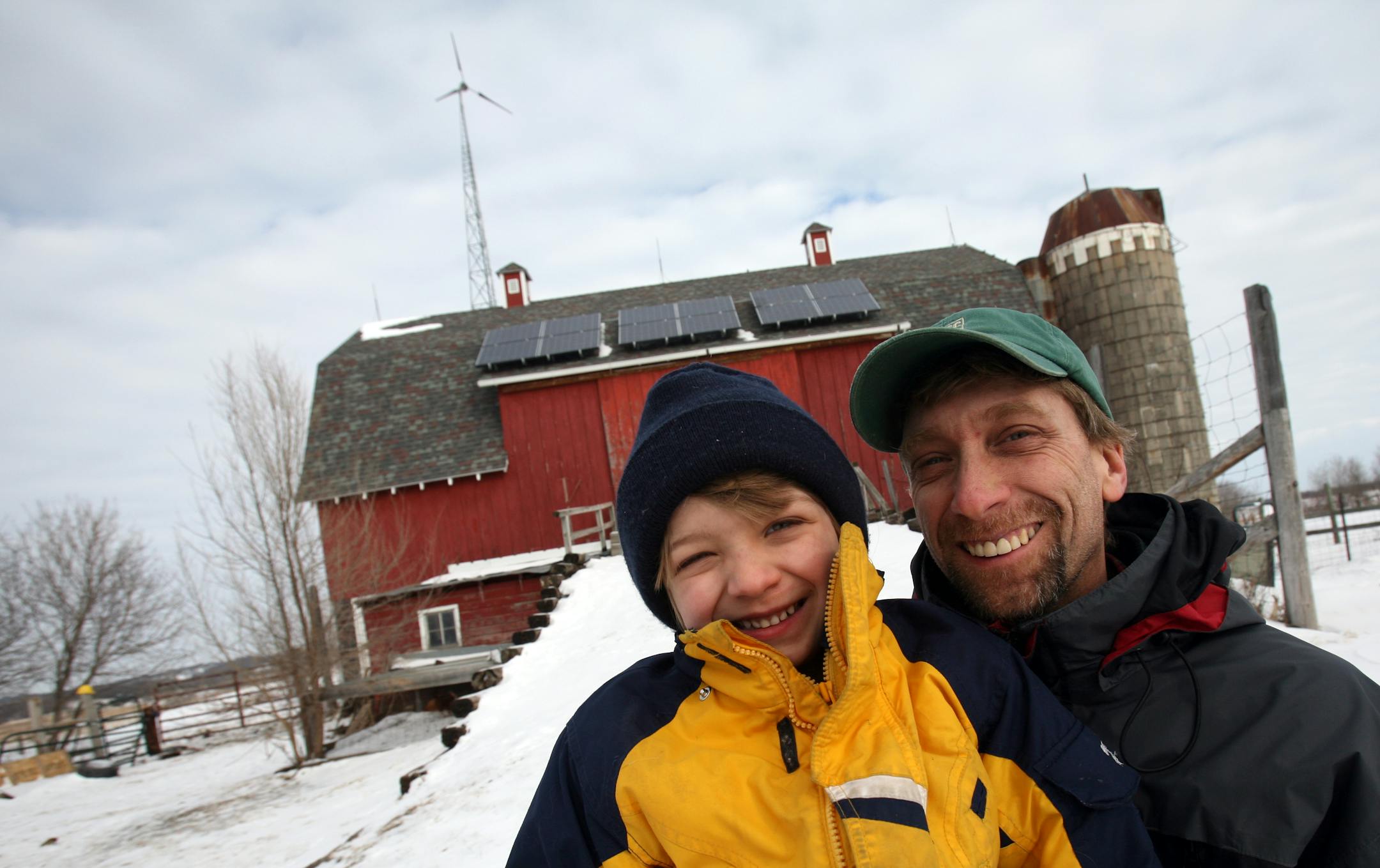 Peter Hark and his son Alden, 6, stood in front of their barn with solar panels and a wind turbine at their hobby farm near Lonsdale. With these alternate energy sources the family hopes to only have to use 30 percent of the county's energy.