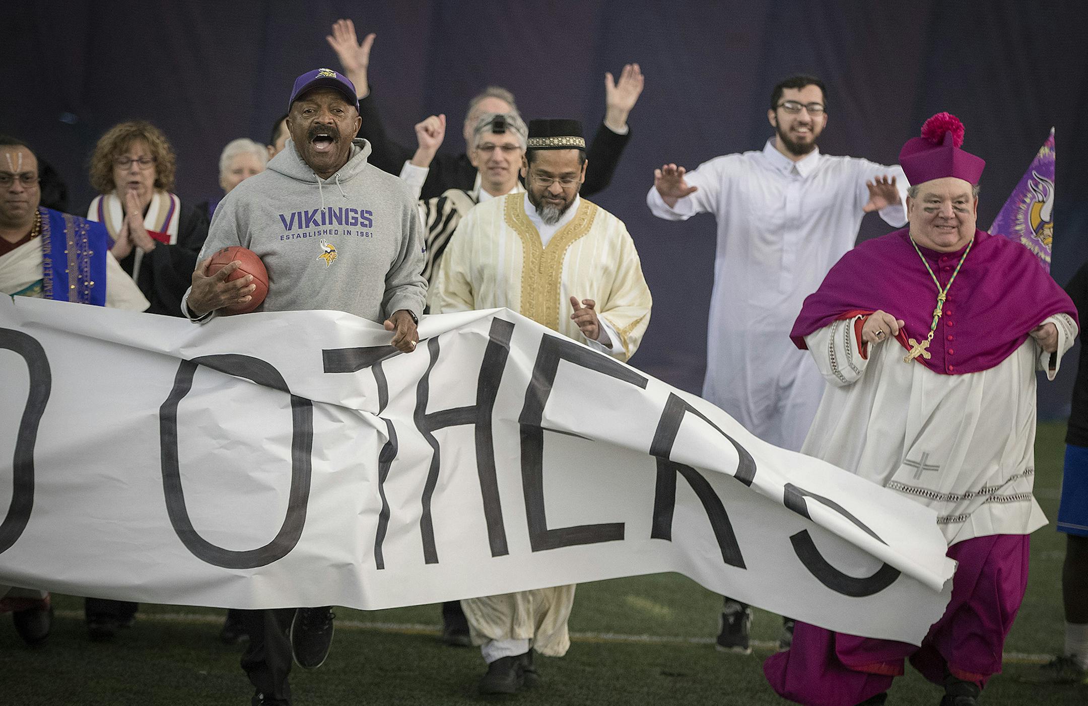 Former Vikings Greg Coleman, left, led local religious leaders Imam Asad Zaman of the Muslim American Society, center, and Archbishop Bernard Hebda, right, on to the field during the filming of a video featuring about 30 religious leaders to benefit the Downtown Congregations to End Homelessness.