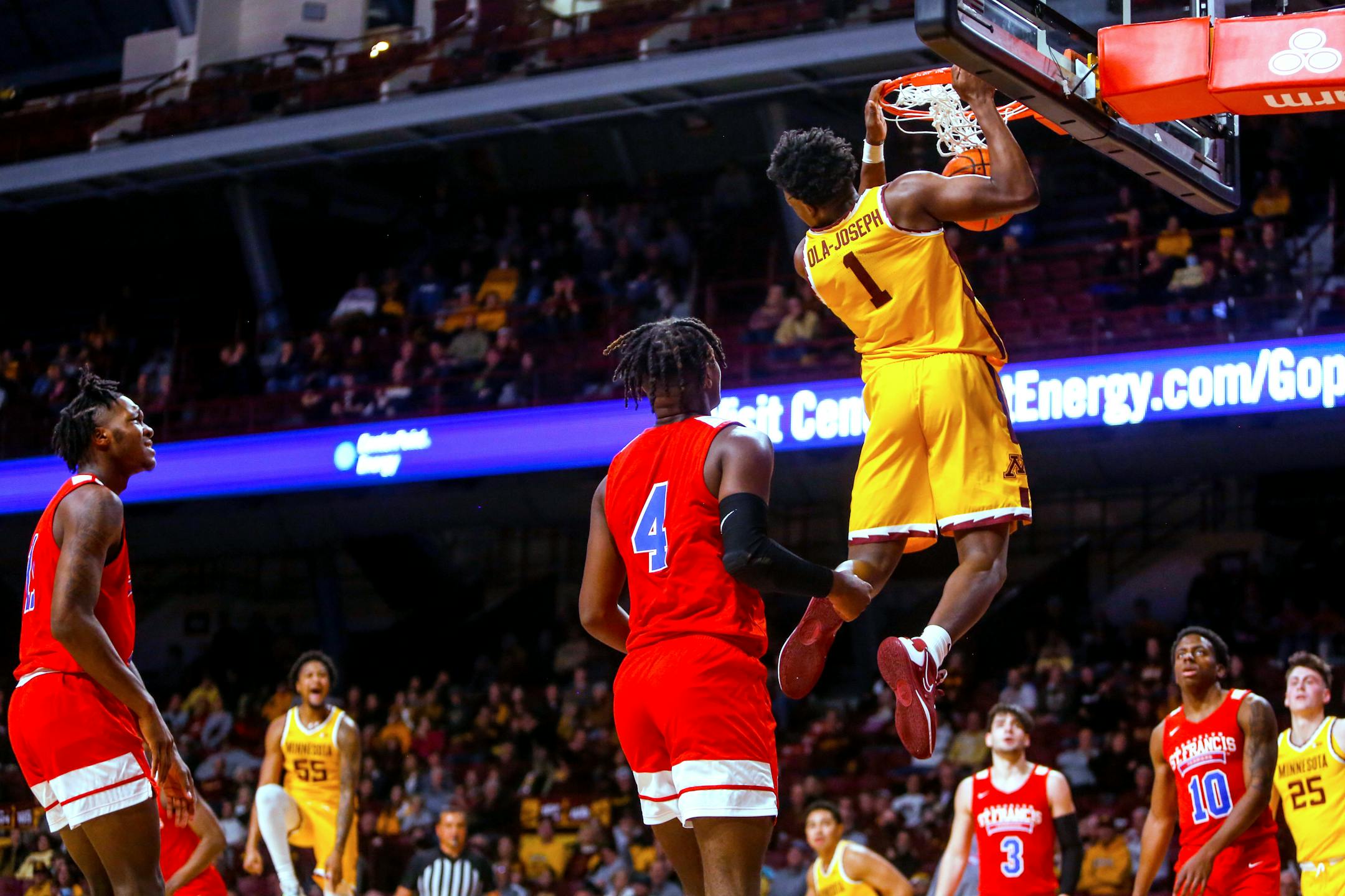 Gophers forward Joshua Ola-Joseph hangs from the basket after dunking against St. Francis Brooklyn  during the first half Friday.