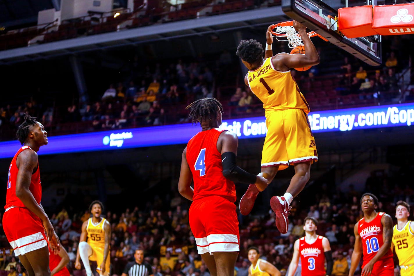 Gophers forward Joshua Ola-Joseph hangs from the basket after dunking against St. Francis Brooklyn  during the first half Friday.