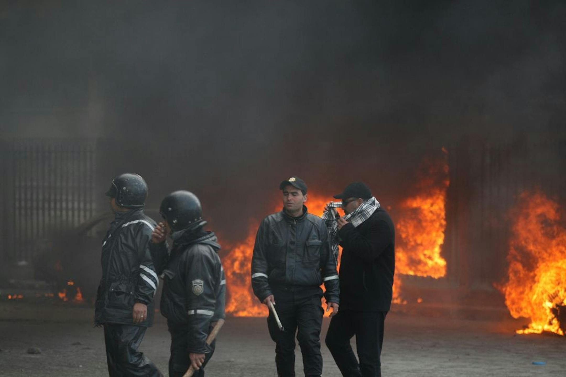 Tunisian police officers stand next to burning cars during clashes earlier this month.