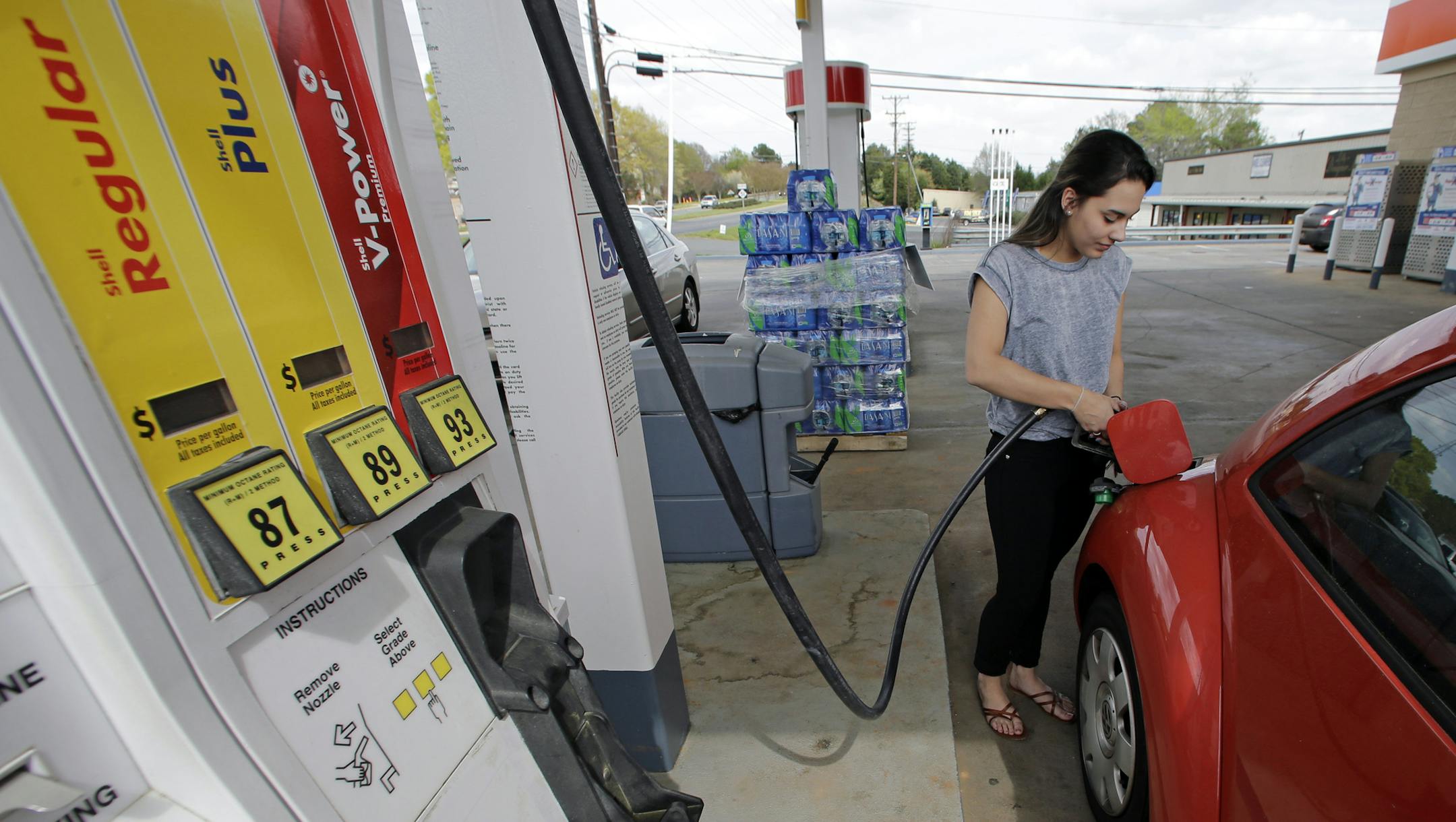 In this April 6, 2015 photo, Lucy Perez, of Charlotte, N.C., pumps gas at a station in Matthews, N.C. A slew of global economic and geopolitical factors are working to pummel the price of oil and set up U.S. drivers for very low gasoline prices later this year. (AP Photo/Chuck Burton)