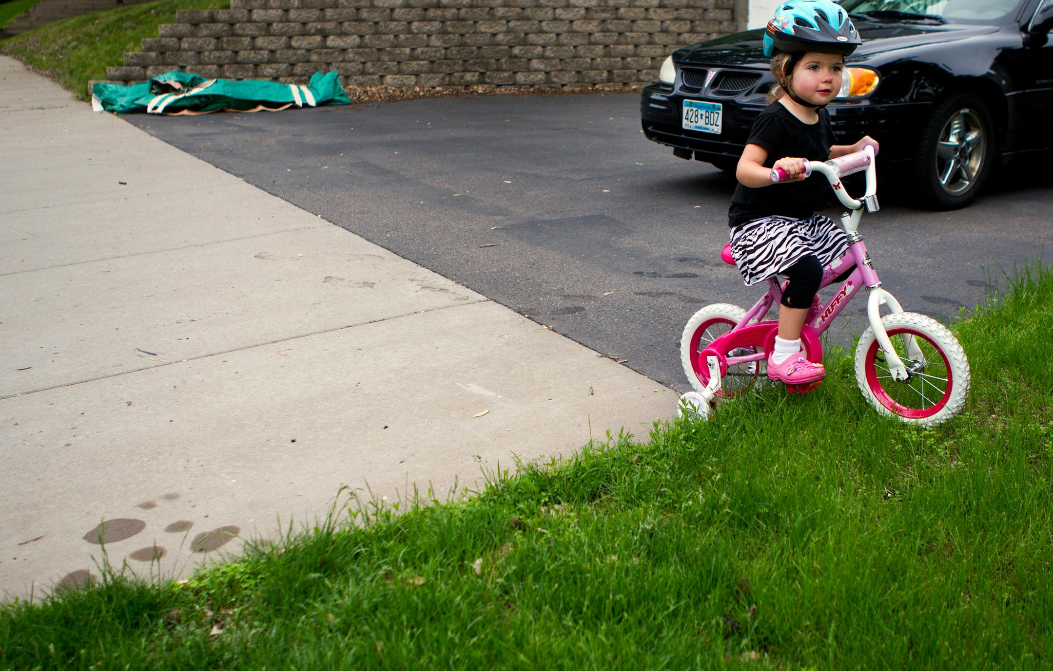 Jada Thate, 3,gets her bike stuck in the grass when the sidewalk ends in her neighborhood in St. Louis Park, Minn., on Thursday, June 6, 2013. Three houses on Zarthan St., including hers, don't have sidewalks in front of their homes. They are scheduled to have sidewalks installed in 2016, but neighbors in the area want the gap filled earlier for safety and social reasons in their neighborhood. ] (ANNA REED/STAR TRIBUNE) anna.reed@startribune.com (cq)