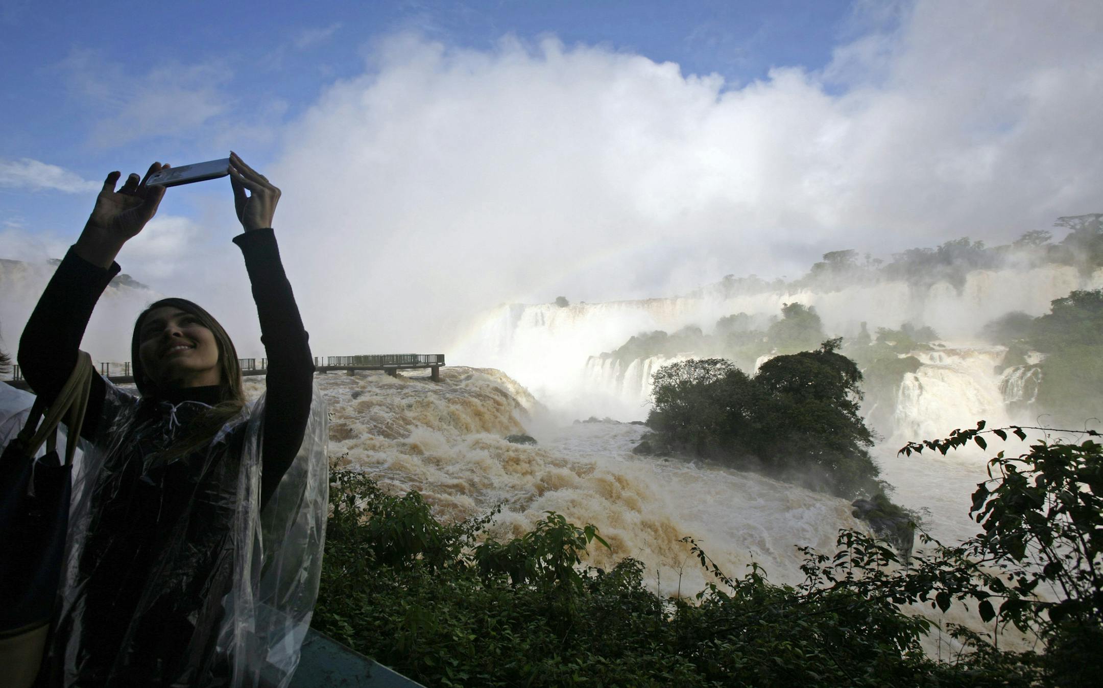 A tourist takes pictures with her cell phone at Iguazu Falls in Iguazu National Park in Brazil, Thursday, June 27, 2013. Torrential rain in the past week in southern Brazil has swollen Iguazu River, obliging authorities to close some of the walkways that lead to the waterfalls known as "Garganta del Diablo," or Devil's Throat. (AP Photo/Jorge Saenz) ORG XMIT: XJS105