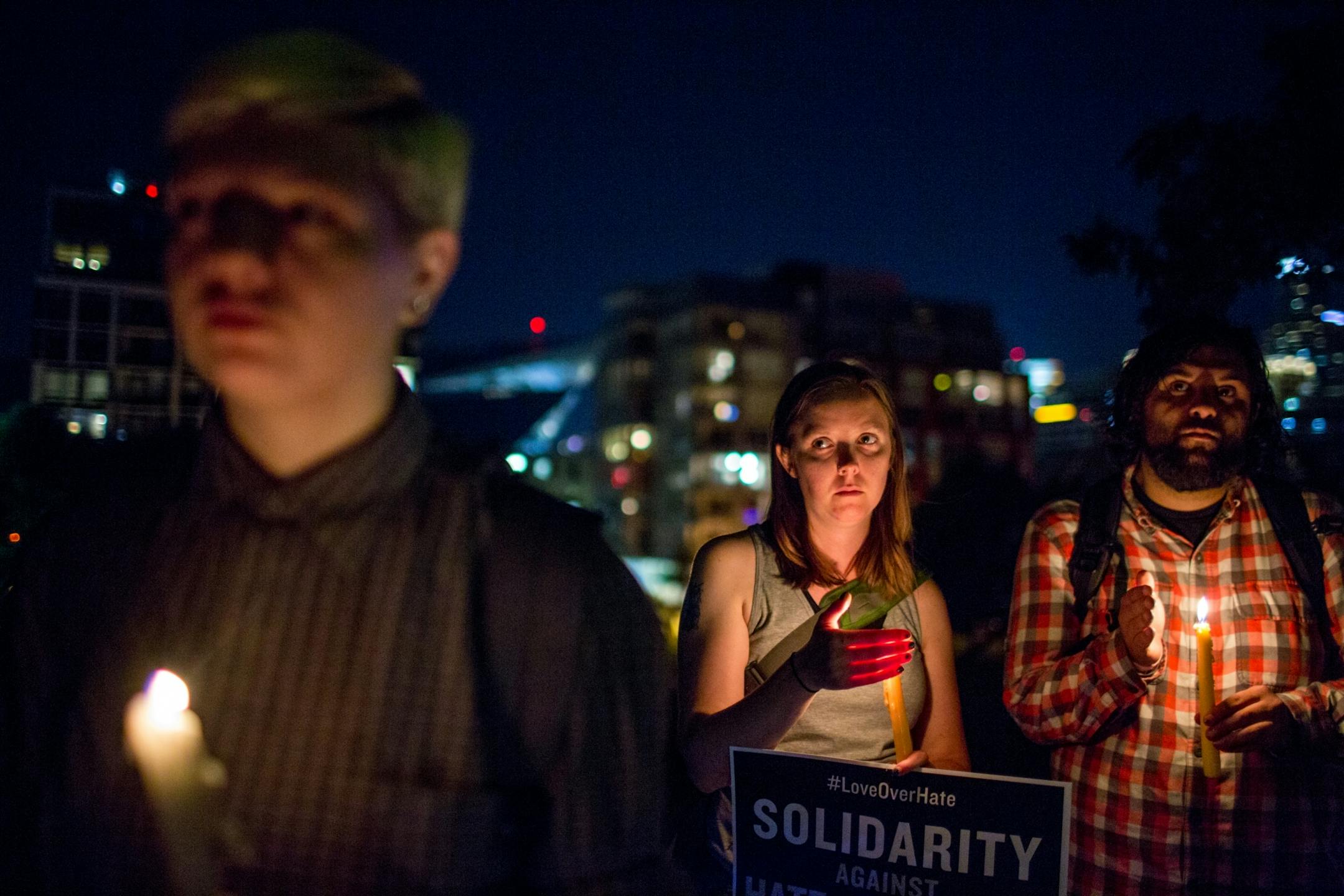 Sam Myers, Emily Christie and Jay Wahi (from left to right) hold candles during a vigil in solidarity with Charlottesville counter protesters at Gold Medal Park, on Saturday night.