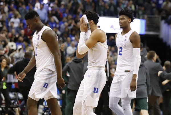 Duke guard Tre Jones, center, covers his face as he walks off the court with teammates Zion Williamson (1) and Cam Reddish (2) after losing to Michiga