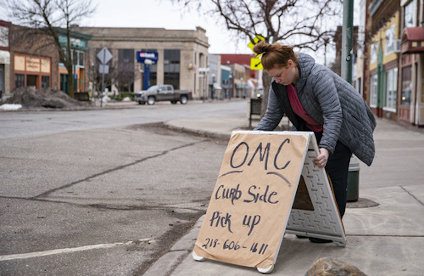 Emma Hirsch place the sign for OMC Smokehouse's curb side pickup on the curb in front of the restaurant on Wednesday morning. ]
ALEX KORMANN &#x2022; alex.kormann@startribune.com OMC Smokehouse remained open on Wednesday for curbside carryout and takeout only. Owner Tom Hanson is preparing for the possibility of a shutdown longer than ten days.