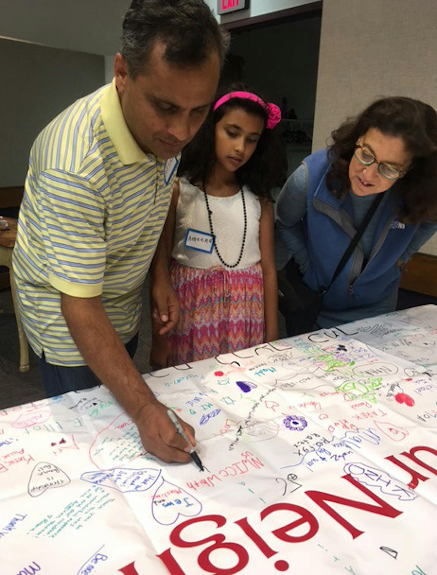 Neyaz Hasan signs a banner with a headline "Love Your Neighbor'' in Urdu and Hindi, as his daughter and Adath Jeshurun member Aimee Orkin look on.