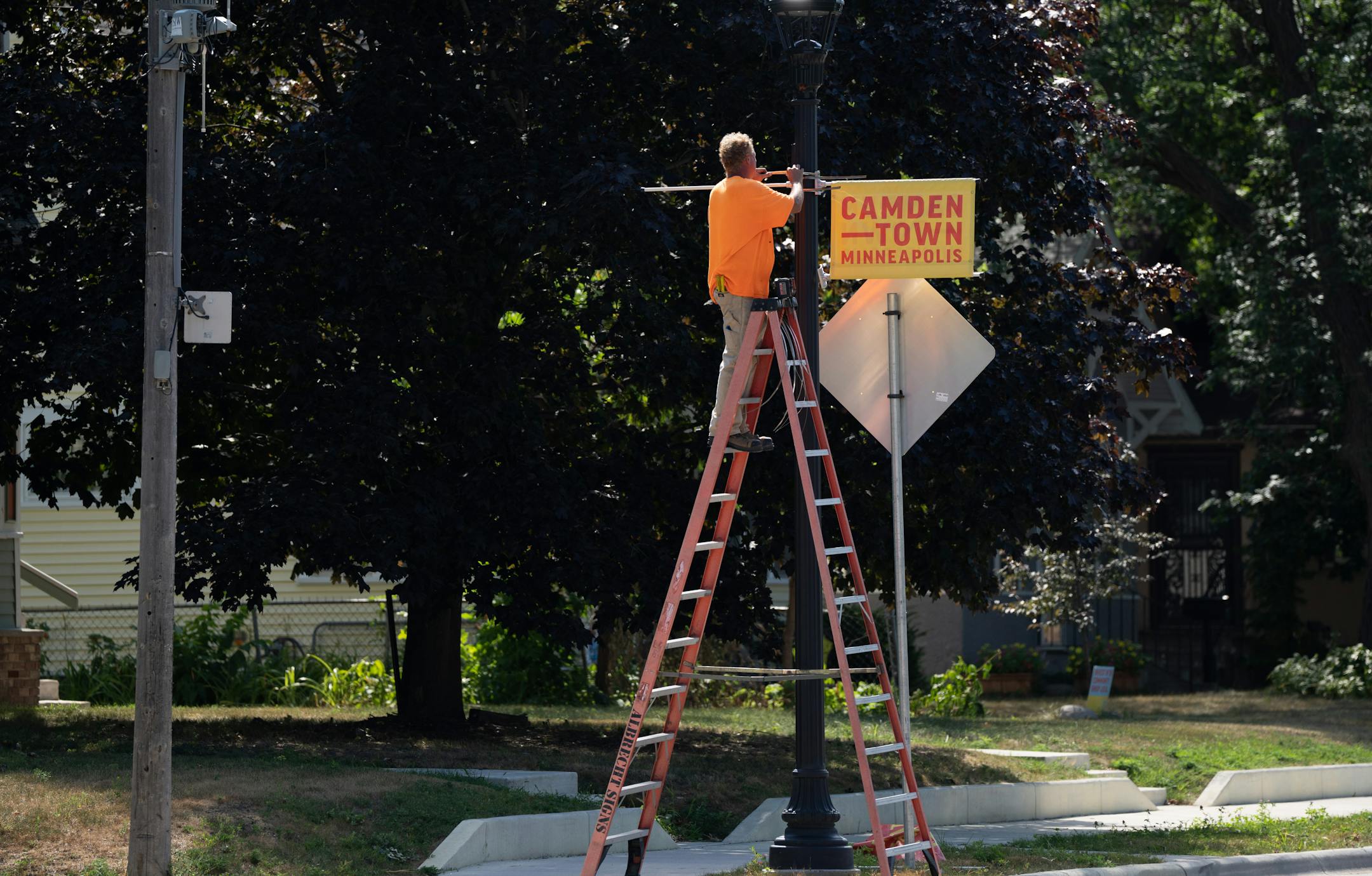 Chris Woodward of Leech Sign Company hangs new Camden Town signs on a street light in Minneapolis.