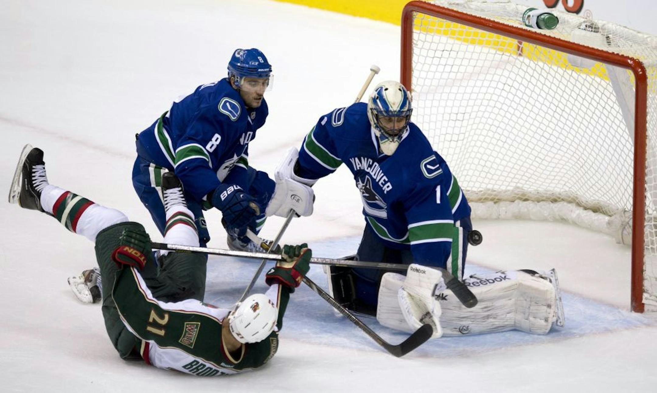Vancouver defenseman Chris Tanev watches as Wild center Kyle Brodziak tries to get a shot past Canucks goalie Roberto Luongo.