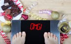 Digital scales with woman feet on them and sign"OMG!" surrounded by christmas decorations, sweets and alcohol. Demonstrates consequences of surfeit an