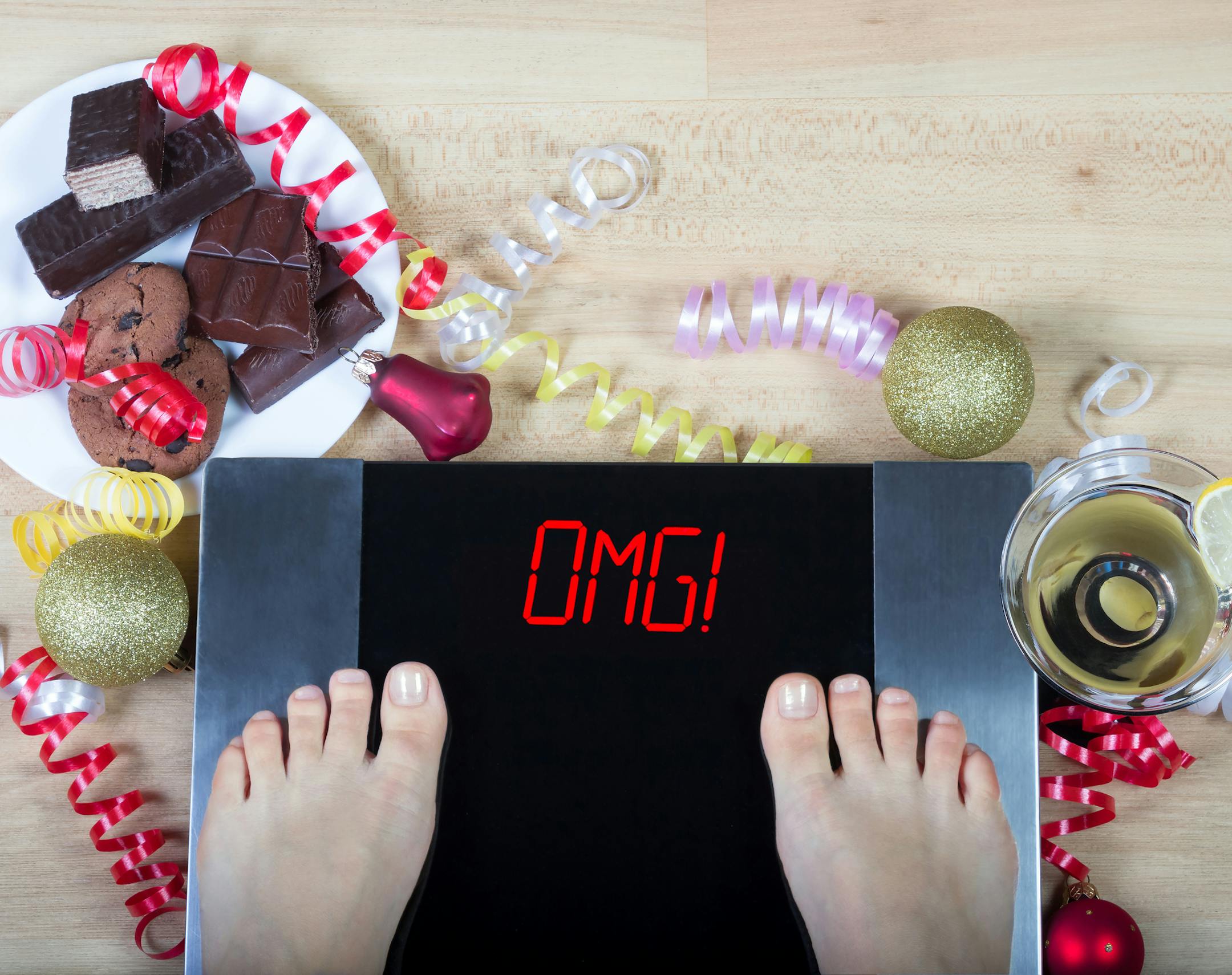 Digital scales with woman feet on them and sign"OMG!" surrounded by christmas decorations, sweets and alcohol. Demonstrates consequences of surfeit and eating unhealthy food during Christmas holidays.