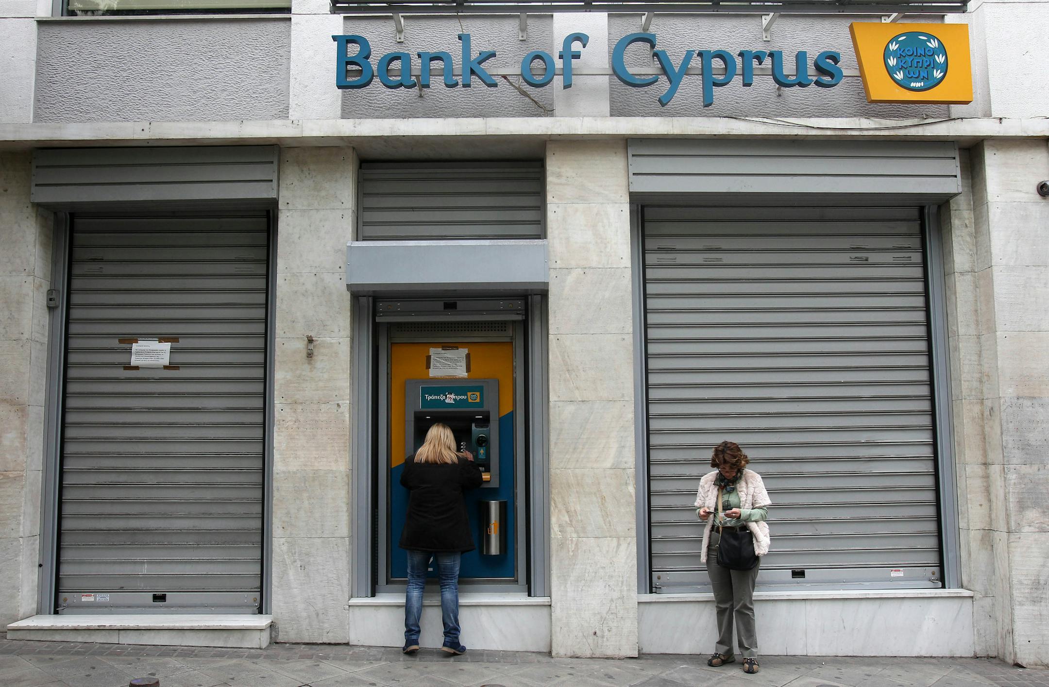 Customers of Bank of Cyprus use the ATM as the bank remains closed for the second day in central Athens on Wednesday, March 20, 2013. Banking stocks in Greece were hammered Tuesday before Cypriot lawmakers rejected a bailout plan, while government officials here urged eurozone countries to give the Mediterranean island more time to come up with a viable solution. (AP Photo/Thanassis Stavrakis)