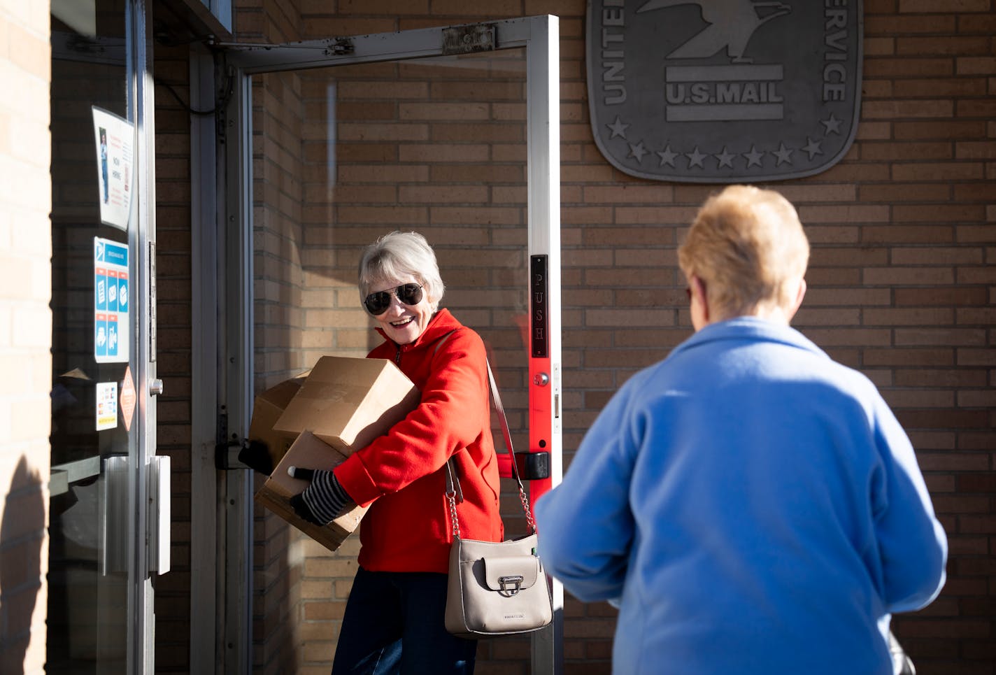 Jeannette Stoks (CQ) holds the door for another customer as she takes a second trip from her car to bring in Christmas packages to deliver at the U.S Post Office on Thursday, Dec. 7, 2023 in downtown Shakopee, Minn. "I got a lot of family out of state," said Stoks. ] RENEE JONES SCHNEIDER • renee.jones@startribune.com