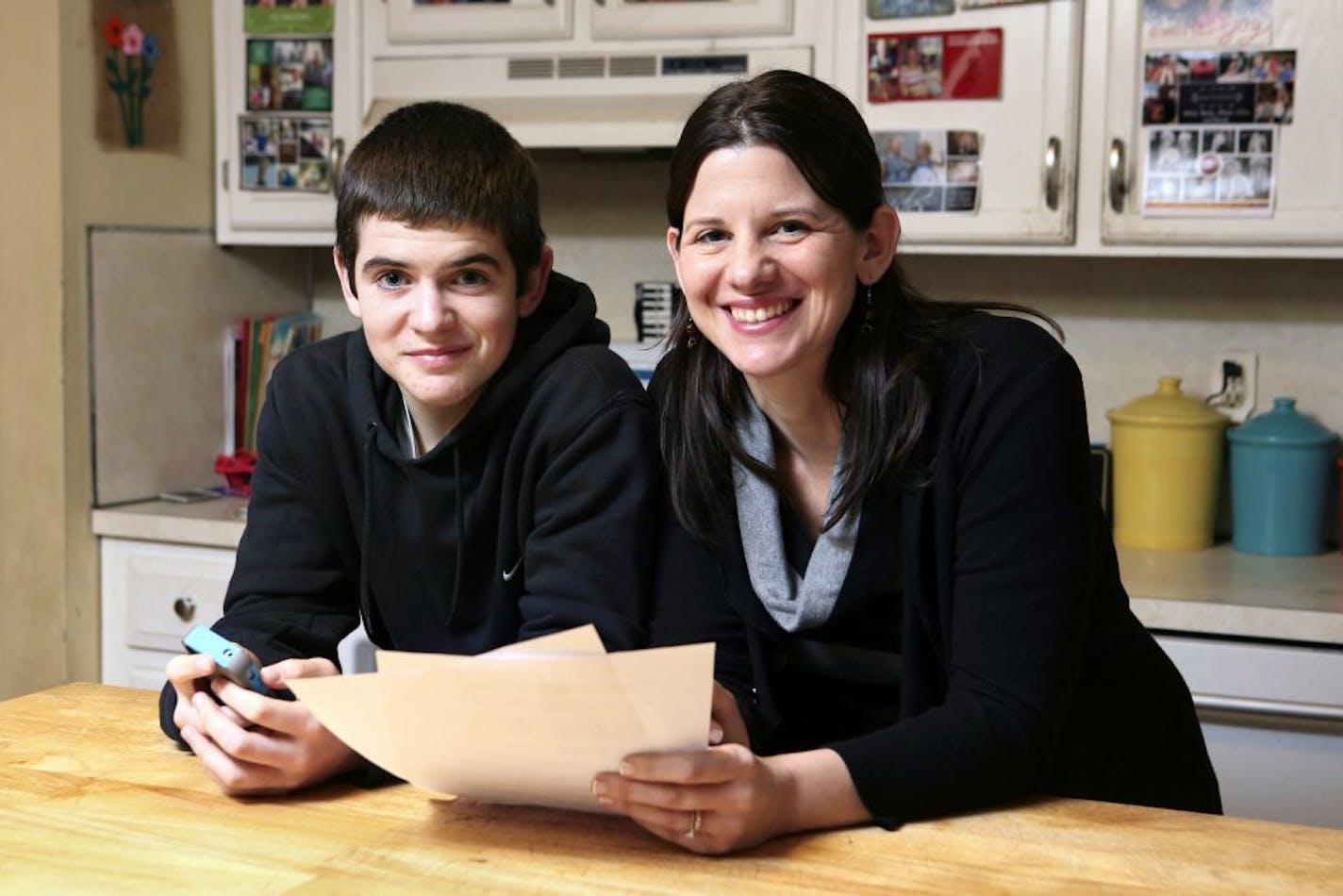 In this Jan. 4, 2013, photo, Janell Burley Hofmann, right, poses with her son Gregory at their home in Sandwich, Mass. Janell holds a copy of the contract she drafted and that Gregory signed as a condition for receiving his first Apple iPhone.