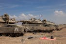 Tanks in a row with solider on top; one has an Israeli flag; on sandy soil with a blue sky with some clouds in the background.
