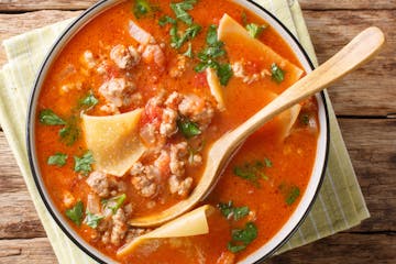 Portion of rich lasagna soup close-up in a plate on the table. Horizontal top view from above