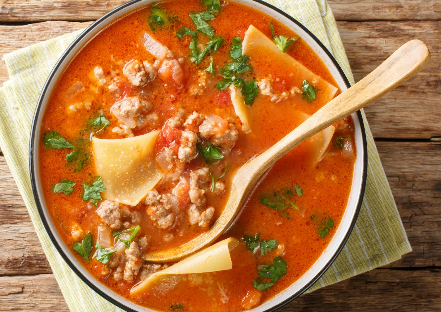 Portion of rich lasagna soup close-up in a plate on the table. Horizontal top view from above