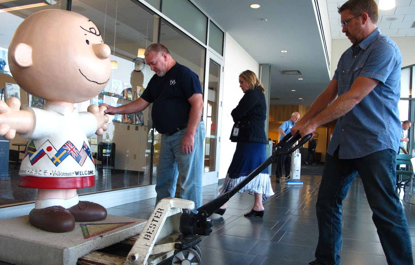 Joe Gullerud, owner, and Scott Fulweiler of Bester Bros. movers of South St. Paul wheeled Charlie Brown into place at the Hardwood Creek county library in Forest Lake. Senior library manager Amy Worwa, center, supervised the final position for the 450-lb. statue.